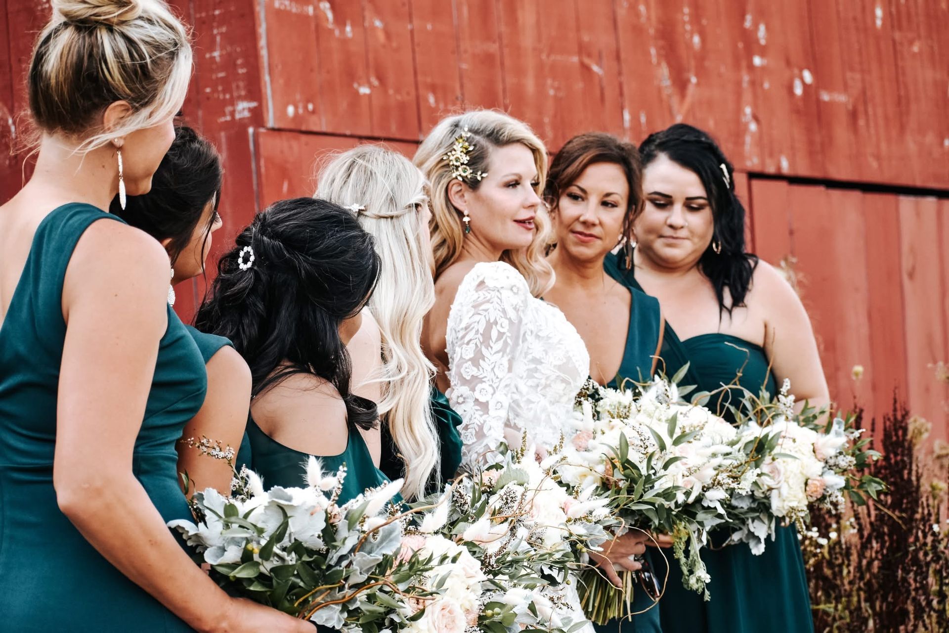 A bride and her bridesmaids are posing for a picture in front of a red barn.