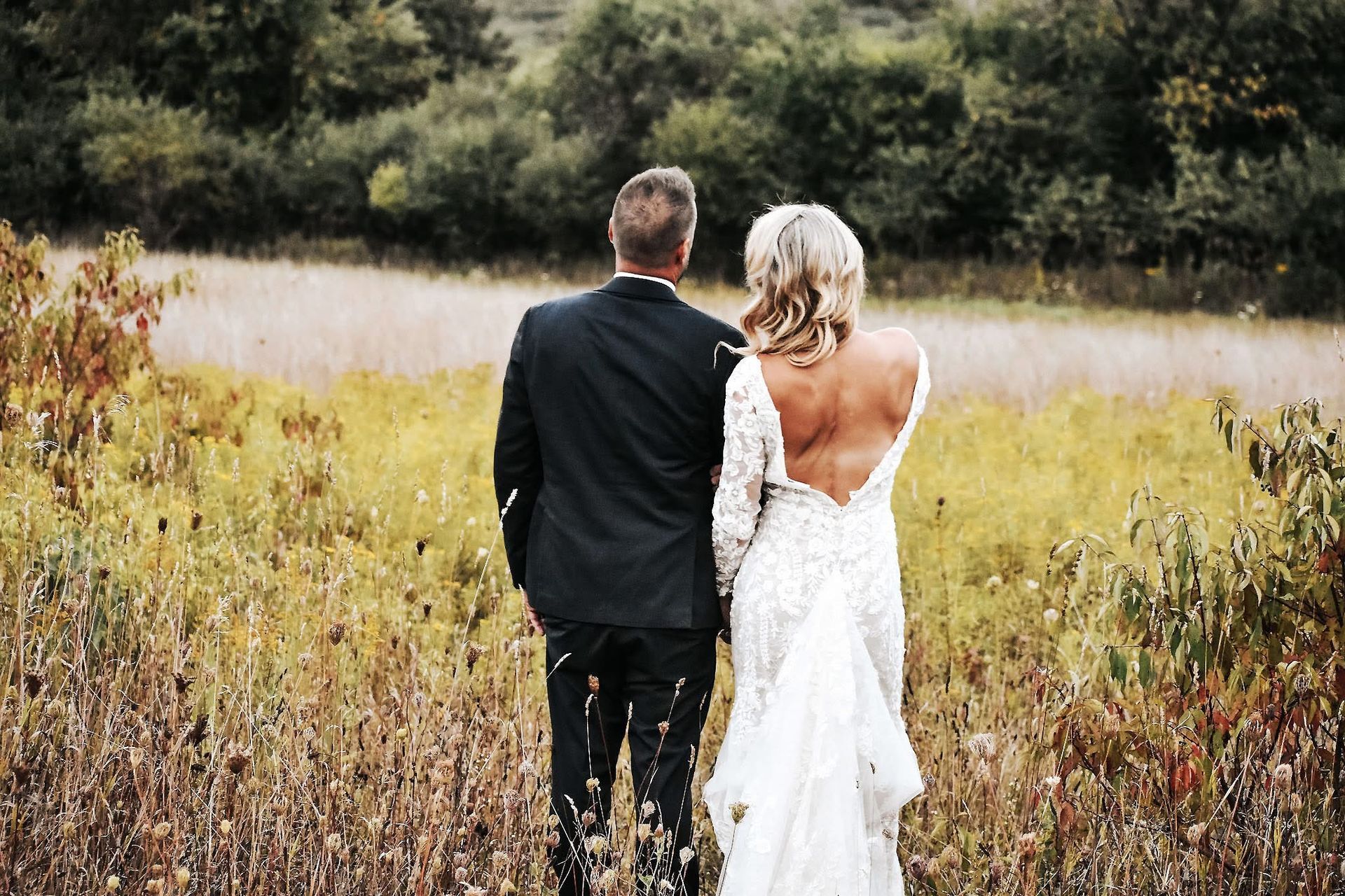 A bride and groom are walking through a field.