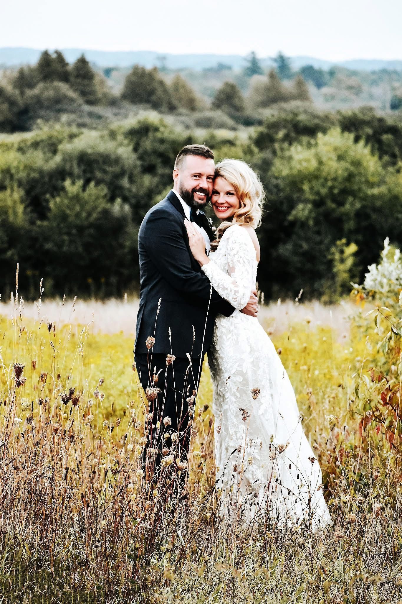 A bride and groom are posing for a picture in a field.