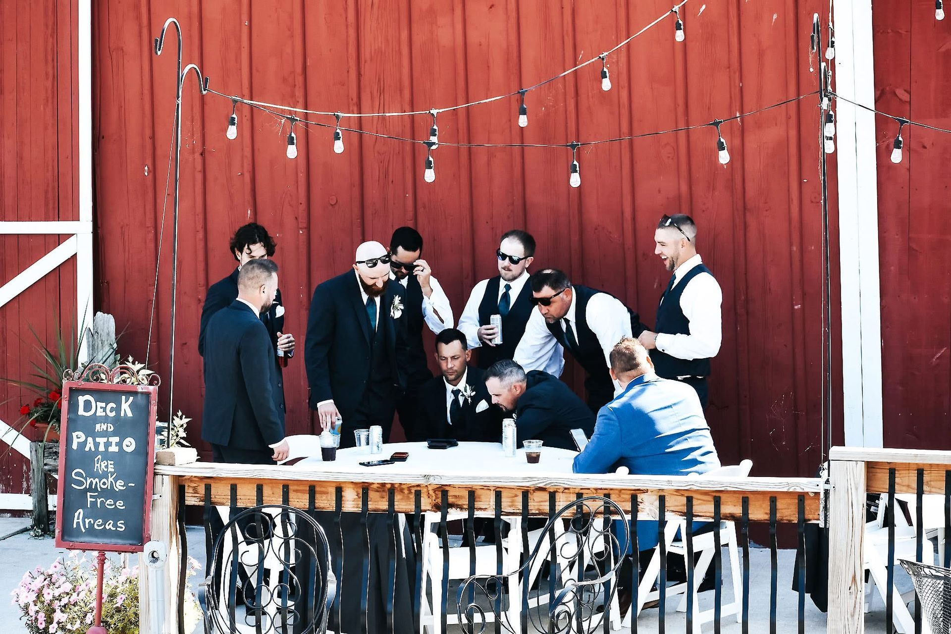 A group of men are standing around a table in front of a red barn.
