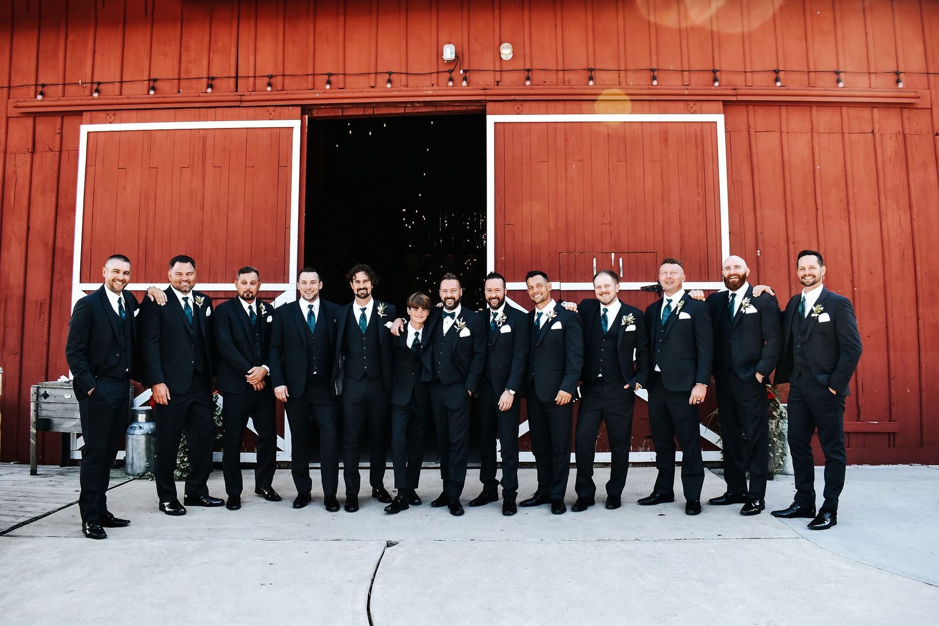 A group of men in suits are posing for a picture in front of a red barn.