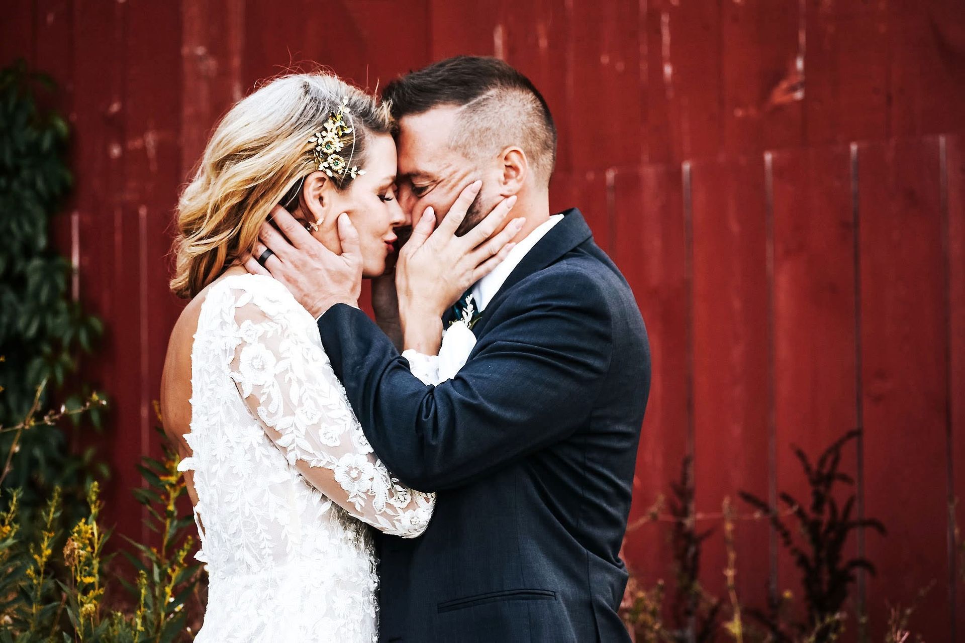 A bride and groom are kissing in front of a red barn.