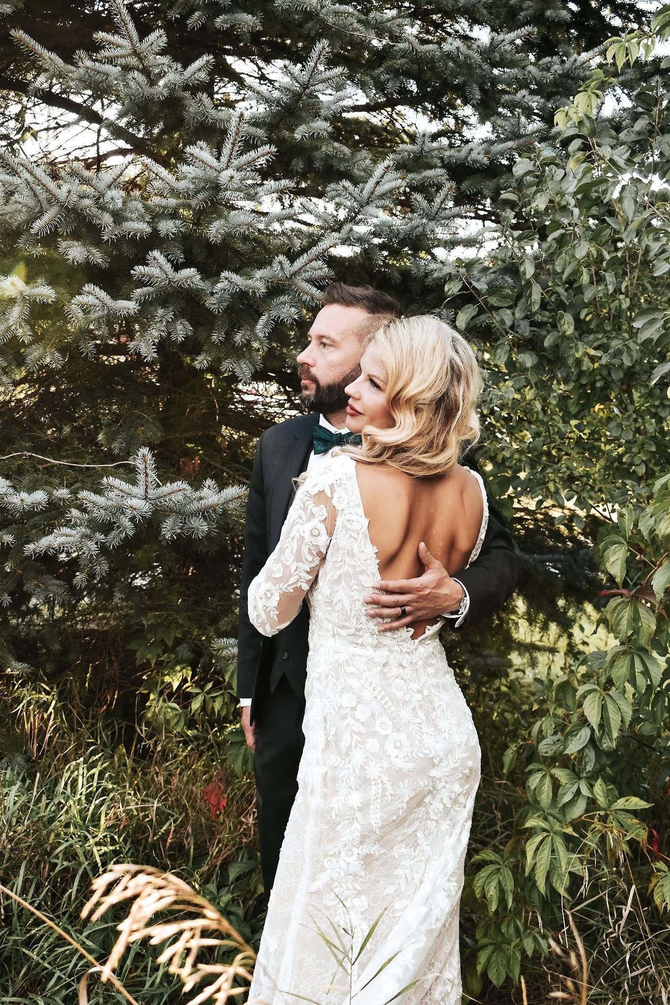 A bride and groom are posing for a picture in front of trees.
