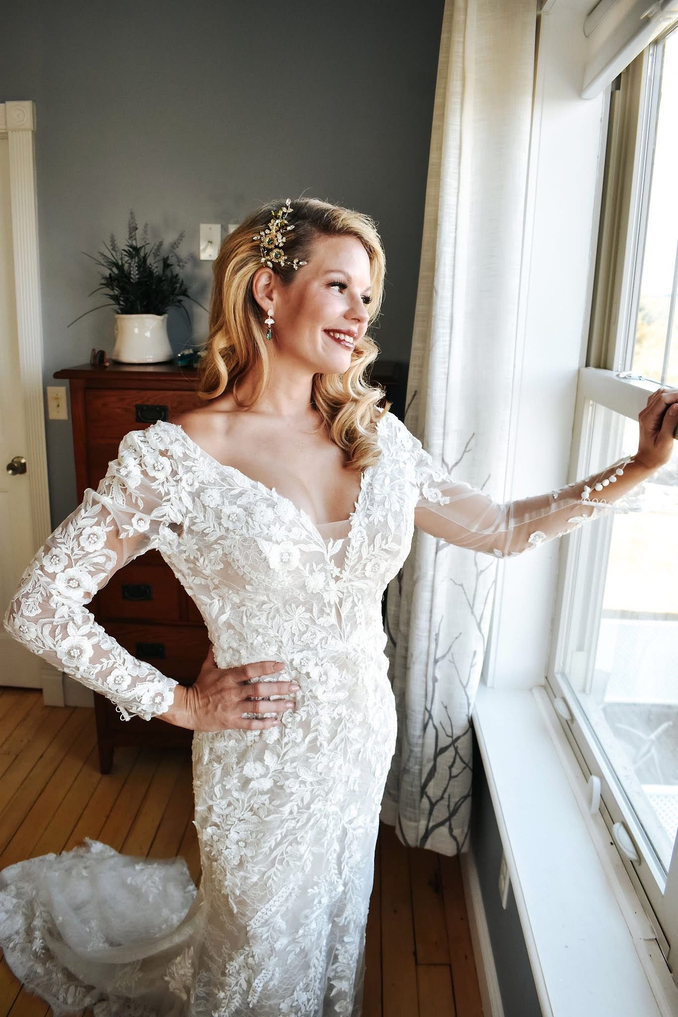 A woman in a wedding dress is standing in front of a window.