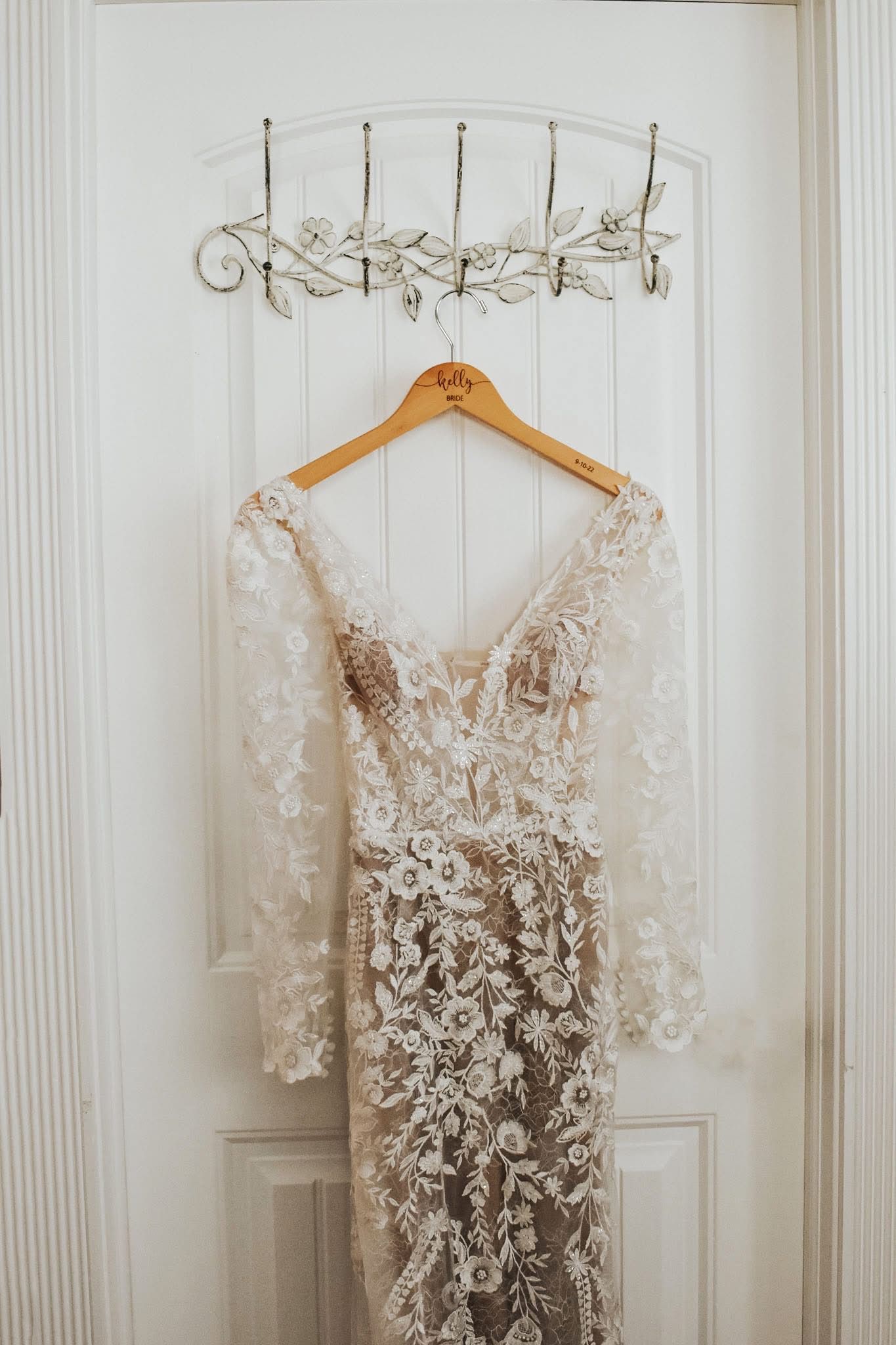 A wedding dress is hanging on a wooden hanger on a door.