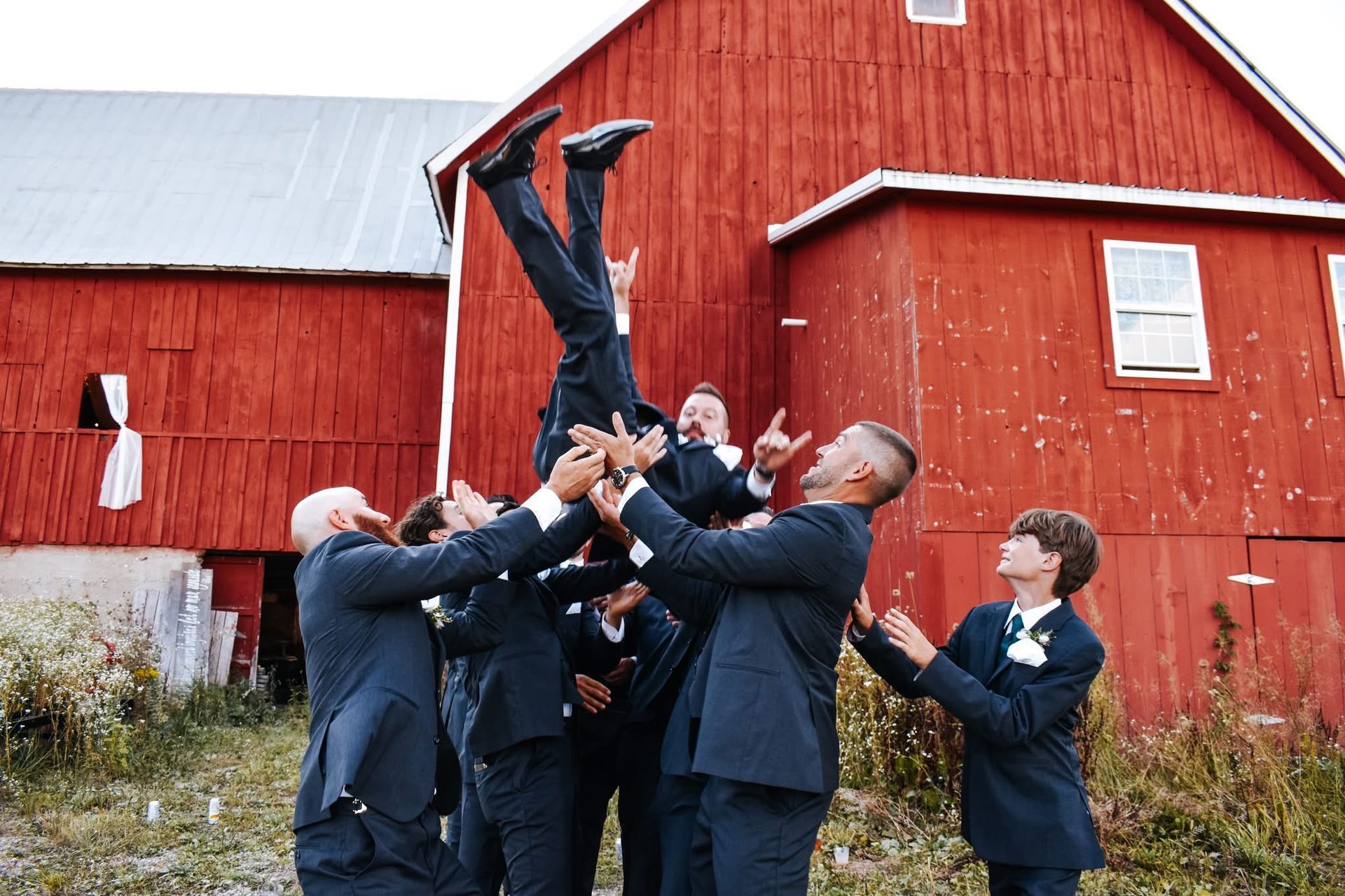 A group of men in suits are standing in front of a red barn.
