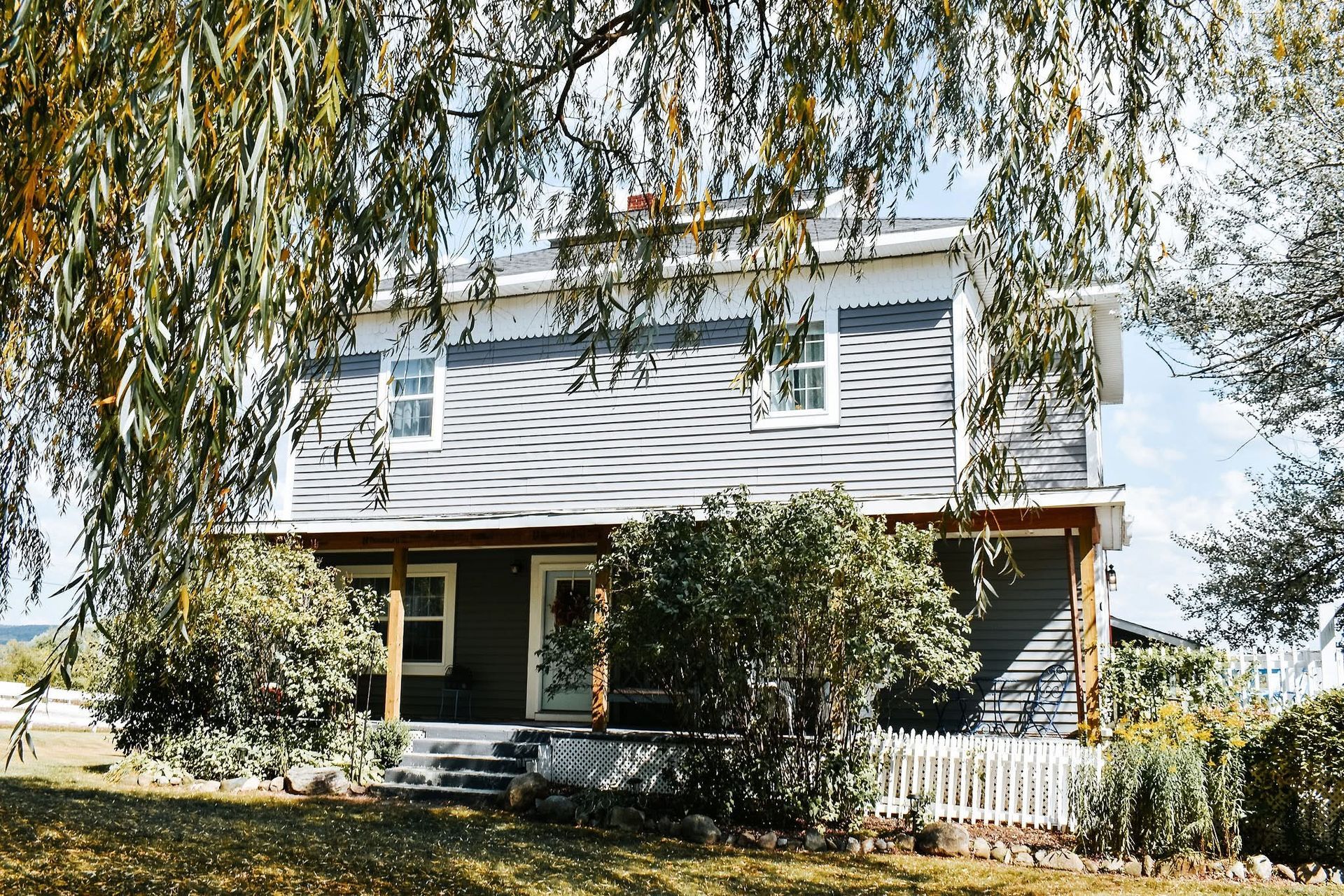 A house with a porch and a tree in front of it.