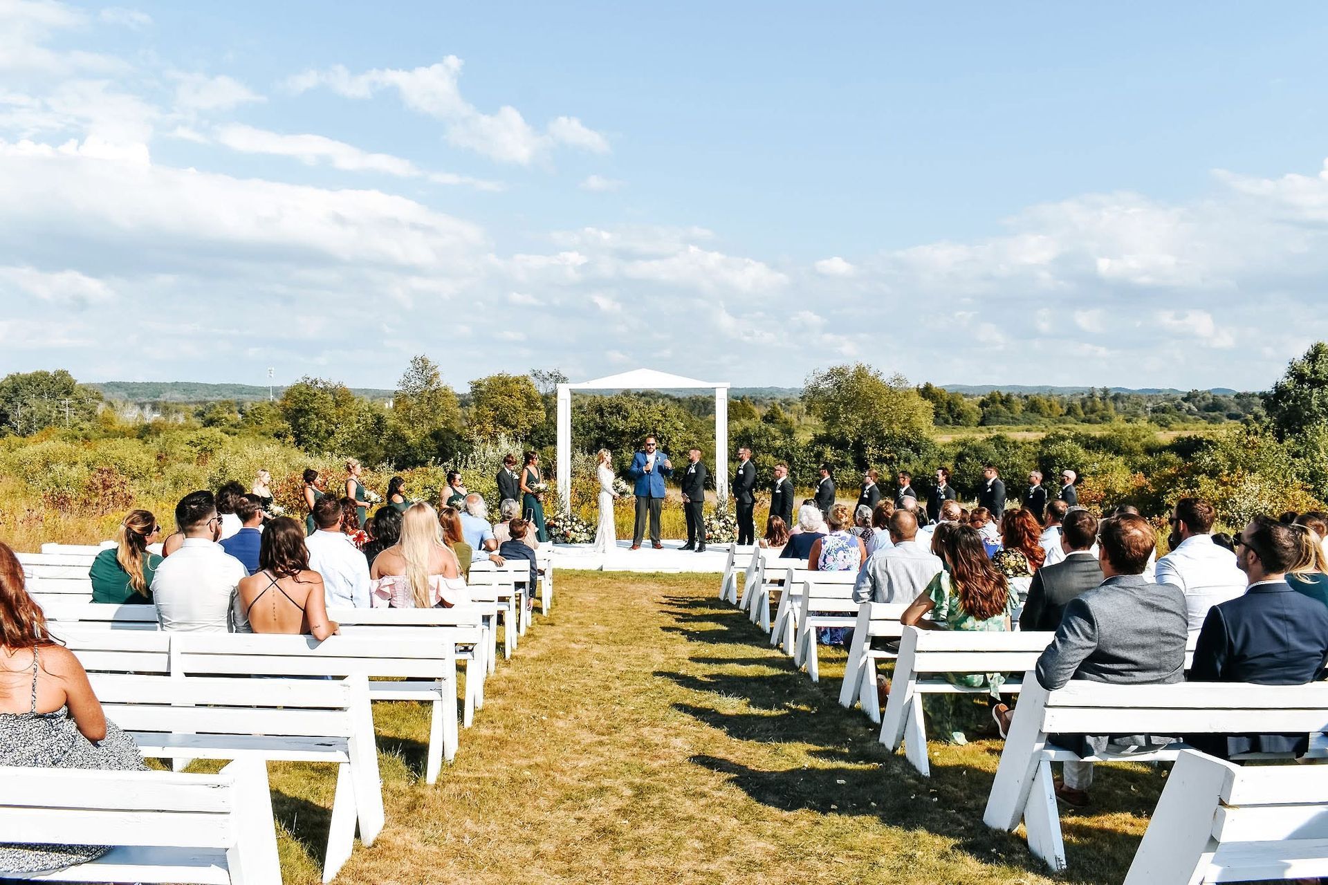 A large group of people are sitting in white chairs at a wedding ceremony.