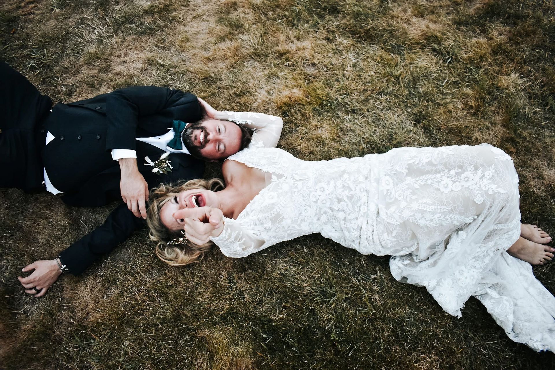 A bride and groom are laying on the grass together.