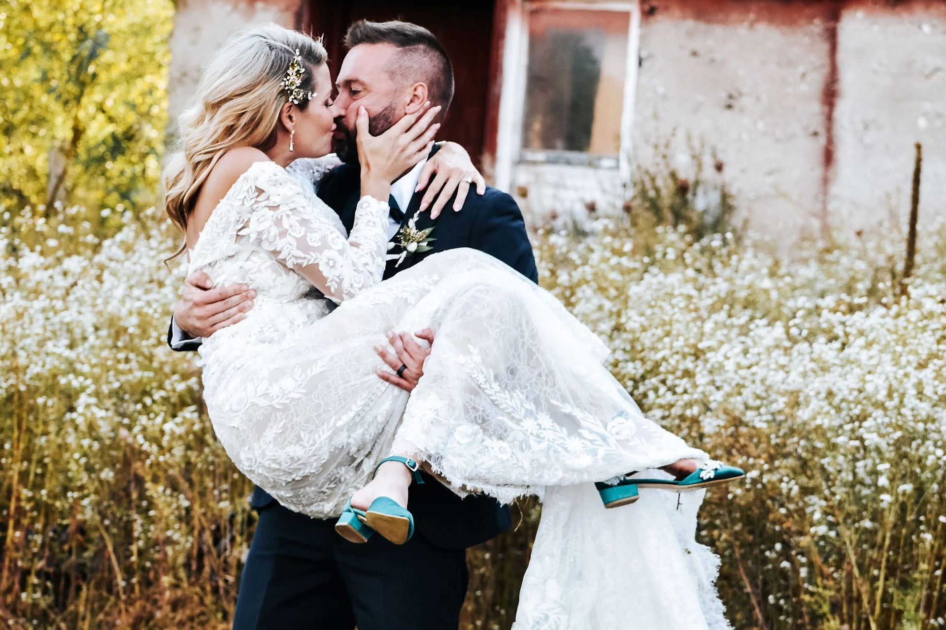 A man is carrying a bride in his arms and they are kissing.