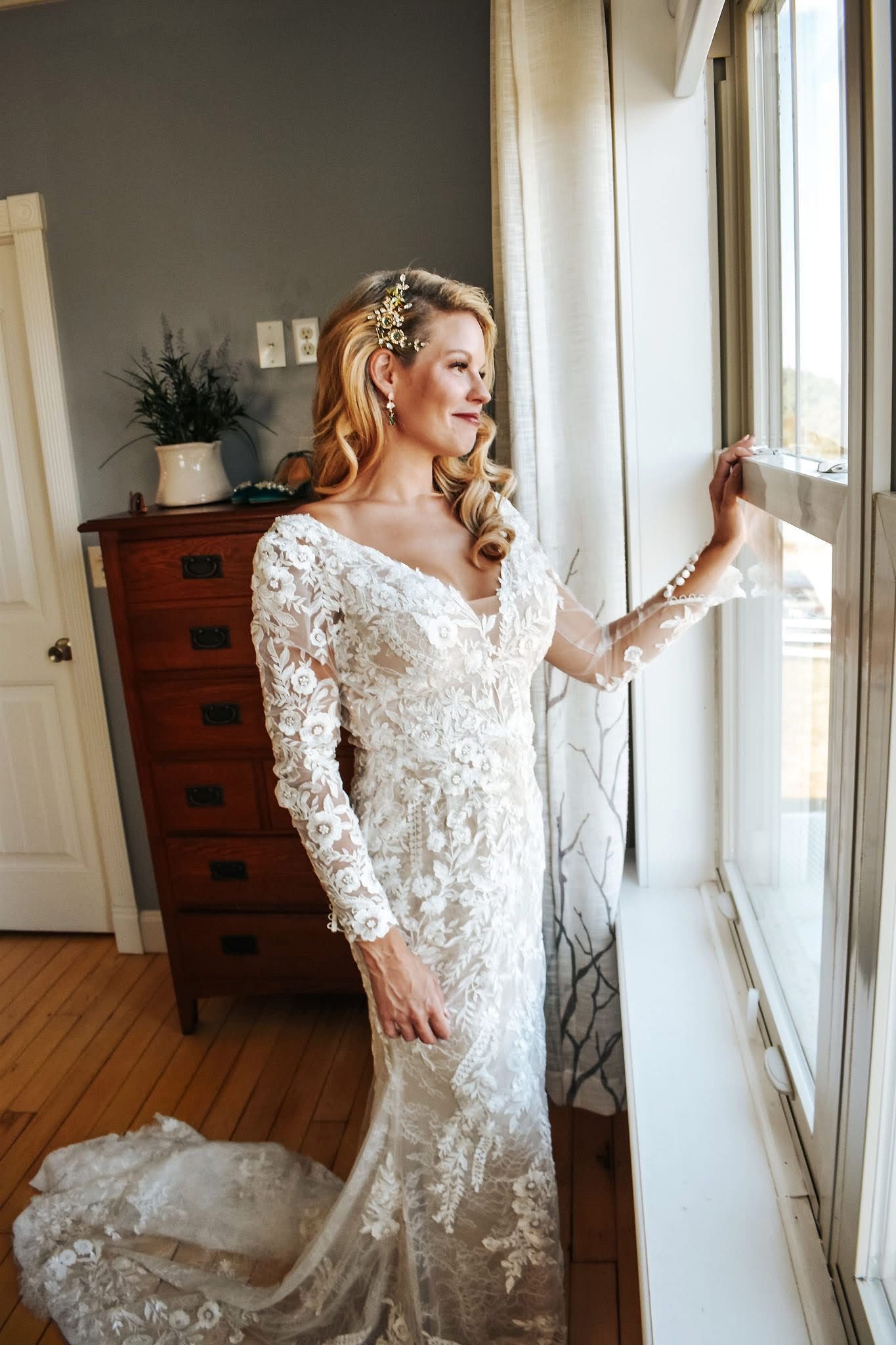 A woman in a wedding dress is standing in front of a window.