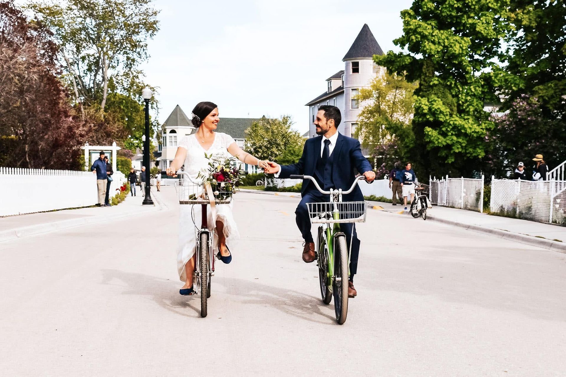 A bride and groom are riding bicycles down a street.