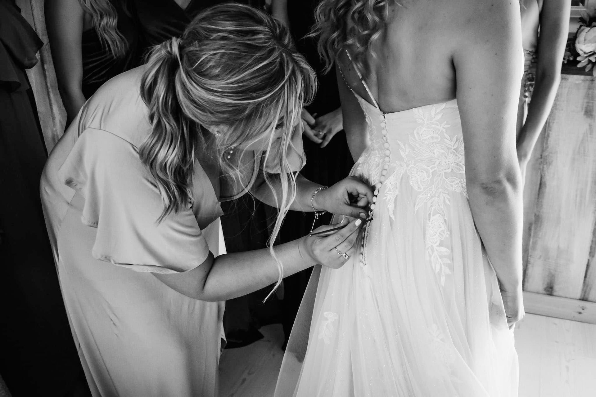 A woman is helping a bride get ready for her wedding in a black and white photo.