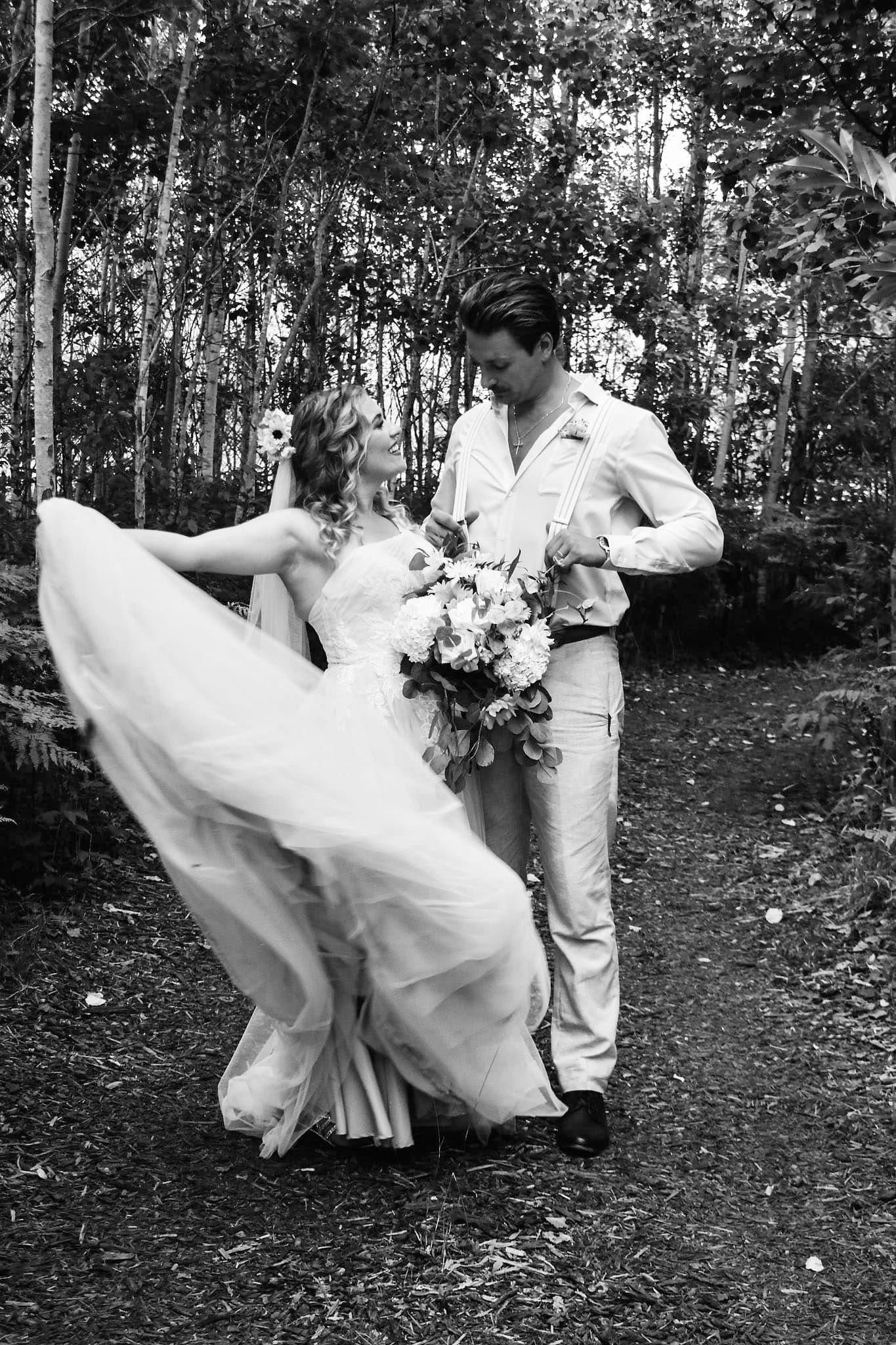 A black and white photo of a bride and groom dancing in the woods.