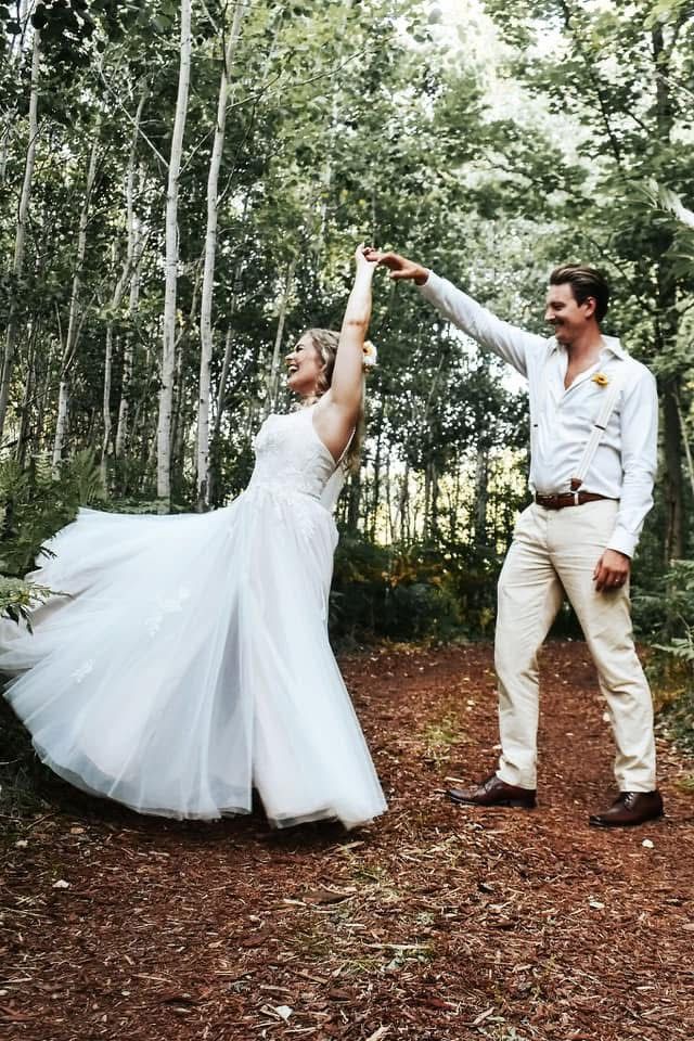 A bride and groom are dancing in the woods.