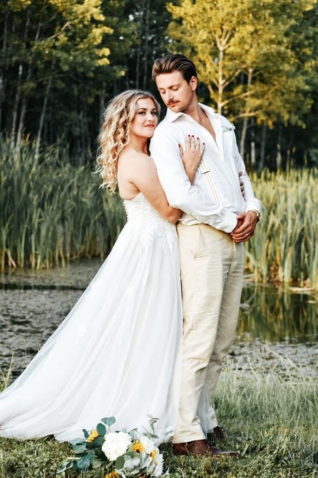 A bride and groom are posing for a picture in front of a pond.