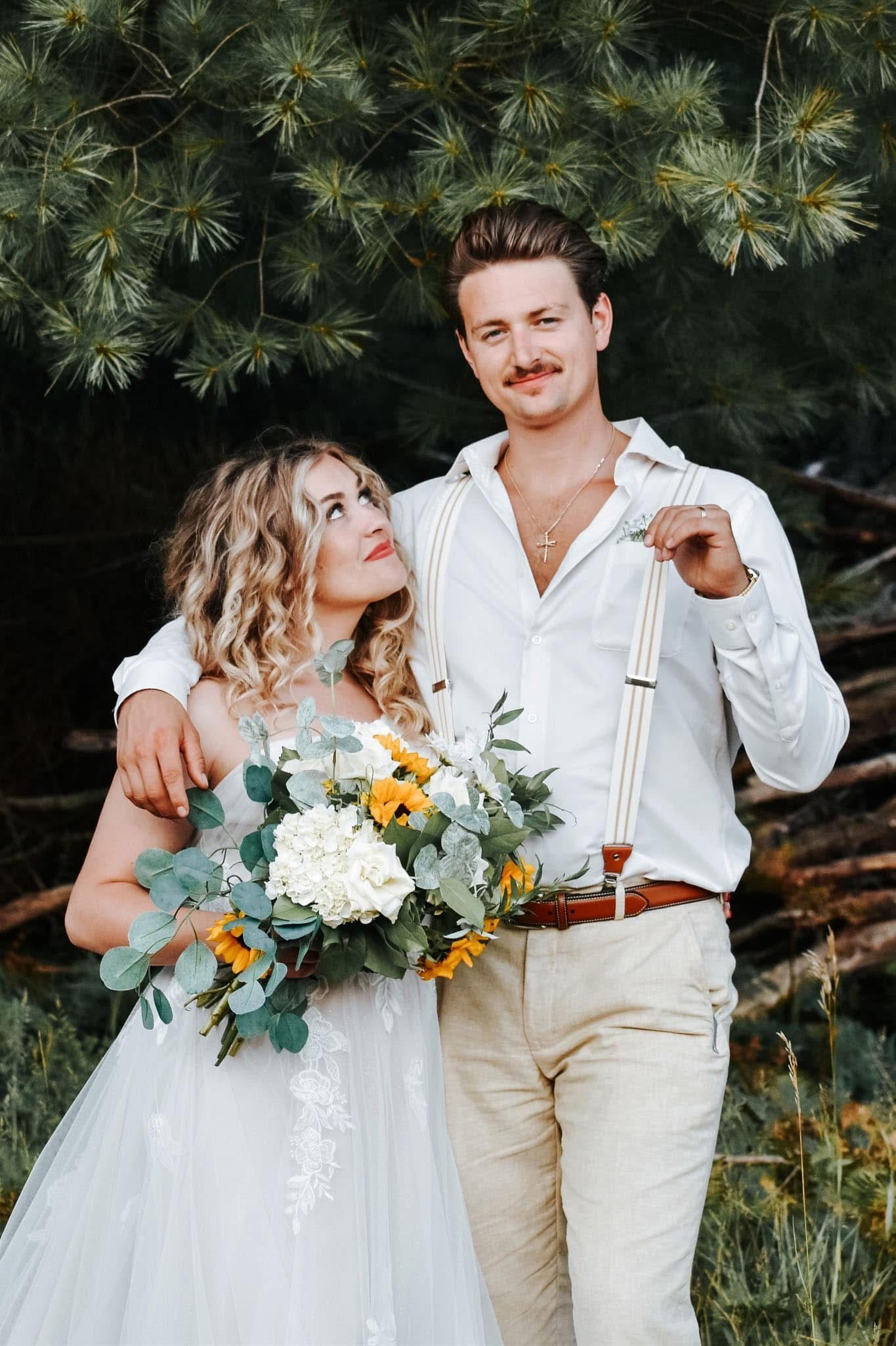 A bride and groom are posing for a picture in front of a pile of logs.