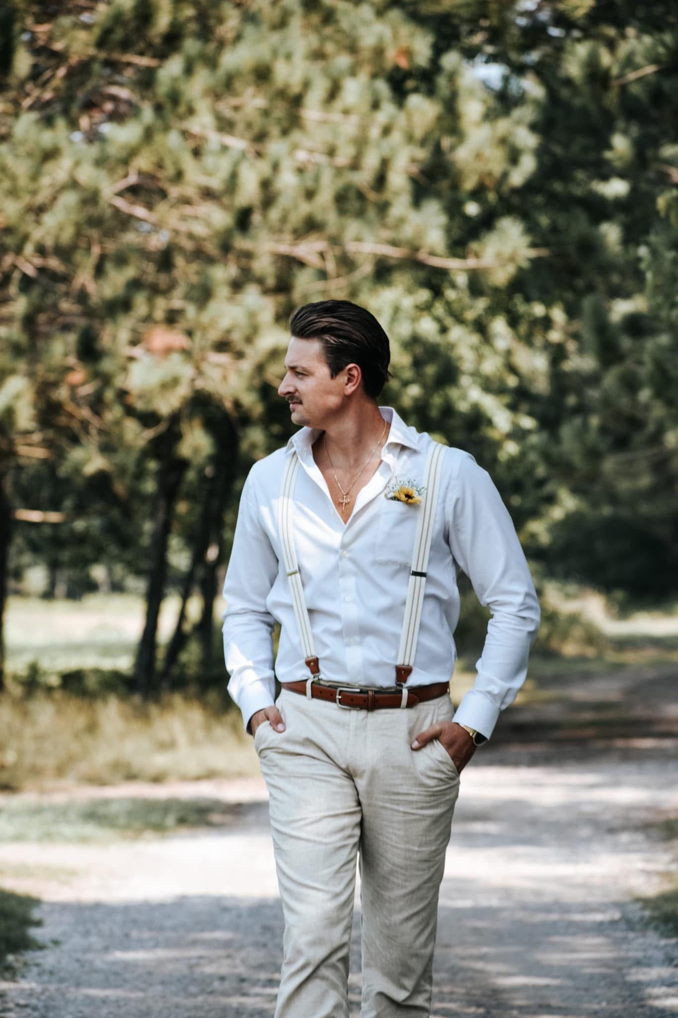 A man in a white shirt and khaki pants is walking down a dirt road.