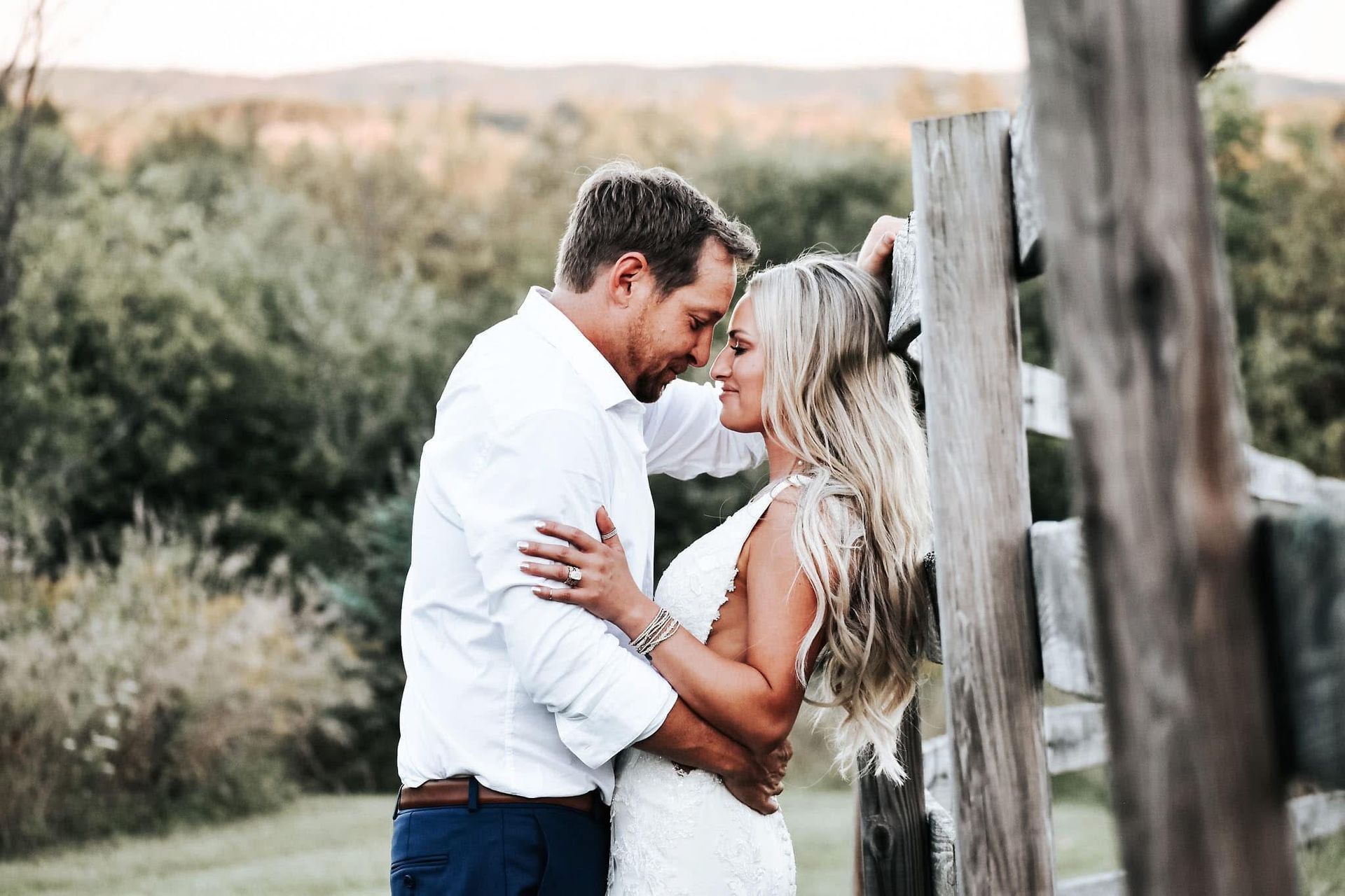A bride and groom are hugging each other while standing next to a wooden fence.
