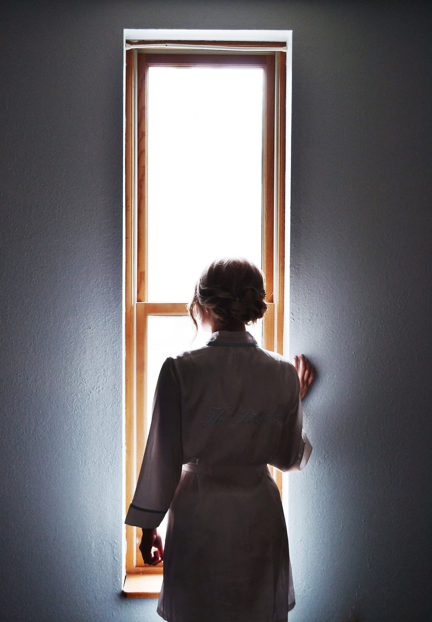 A woman in a robe is looking out a window