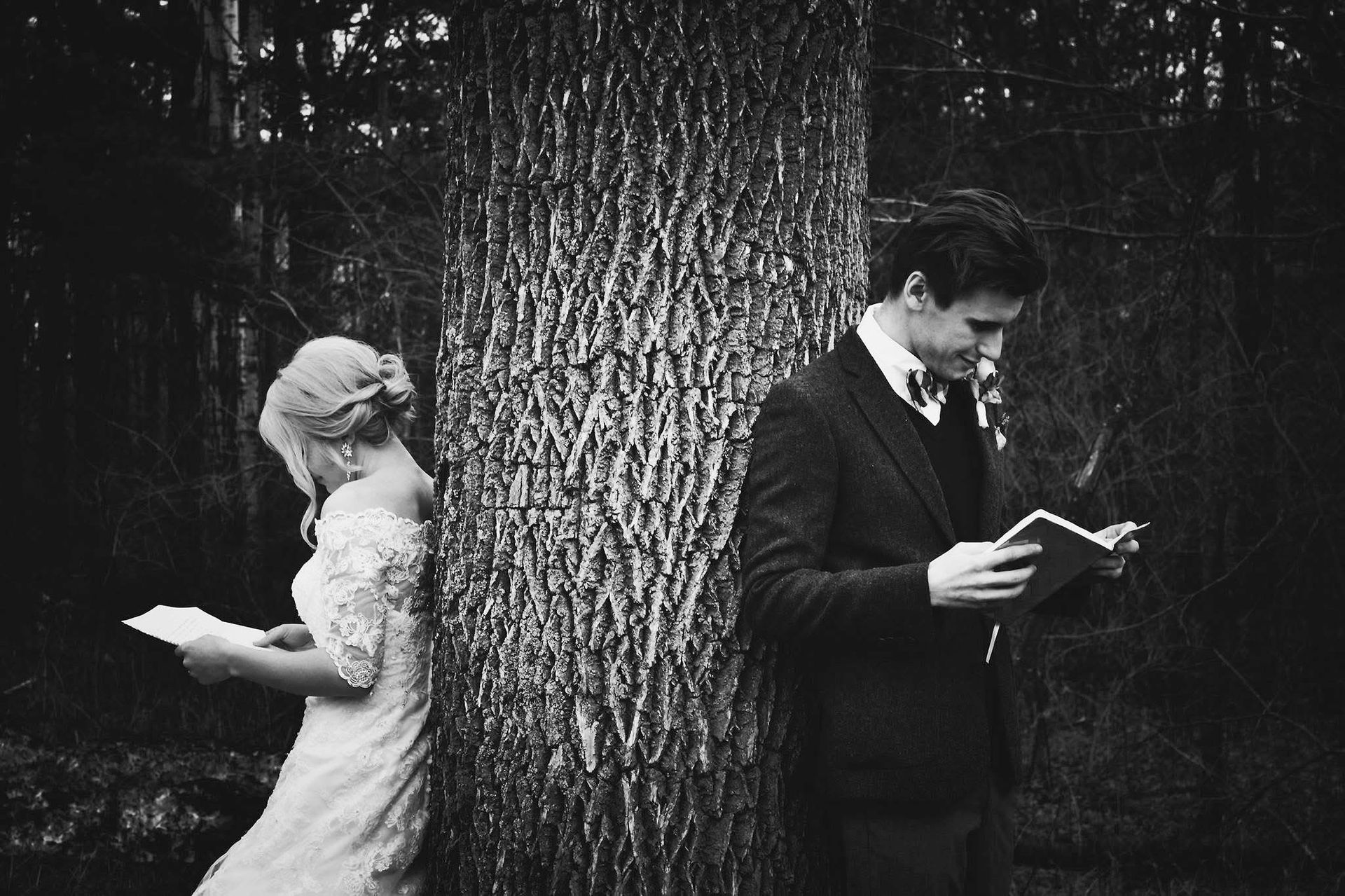 A bride and groom are reading letters in front of a tree.
