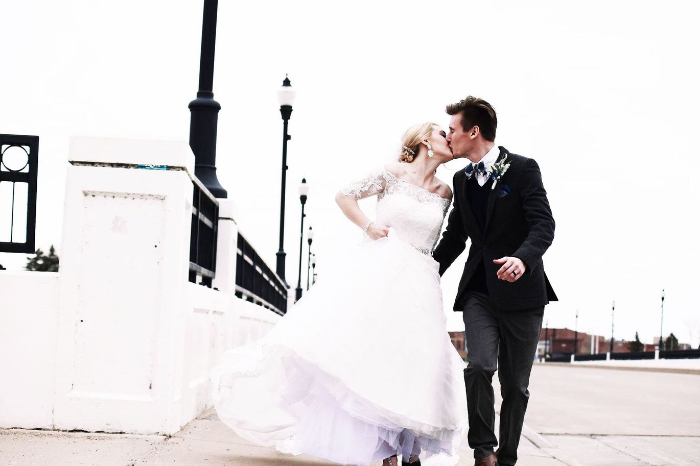 A bride and groom are kissing while walking on a sidewalk.