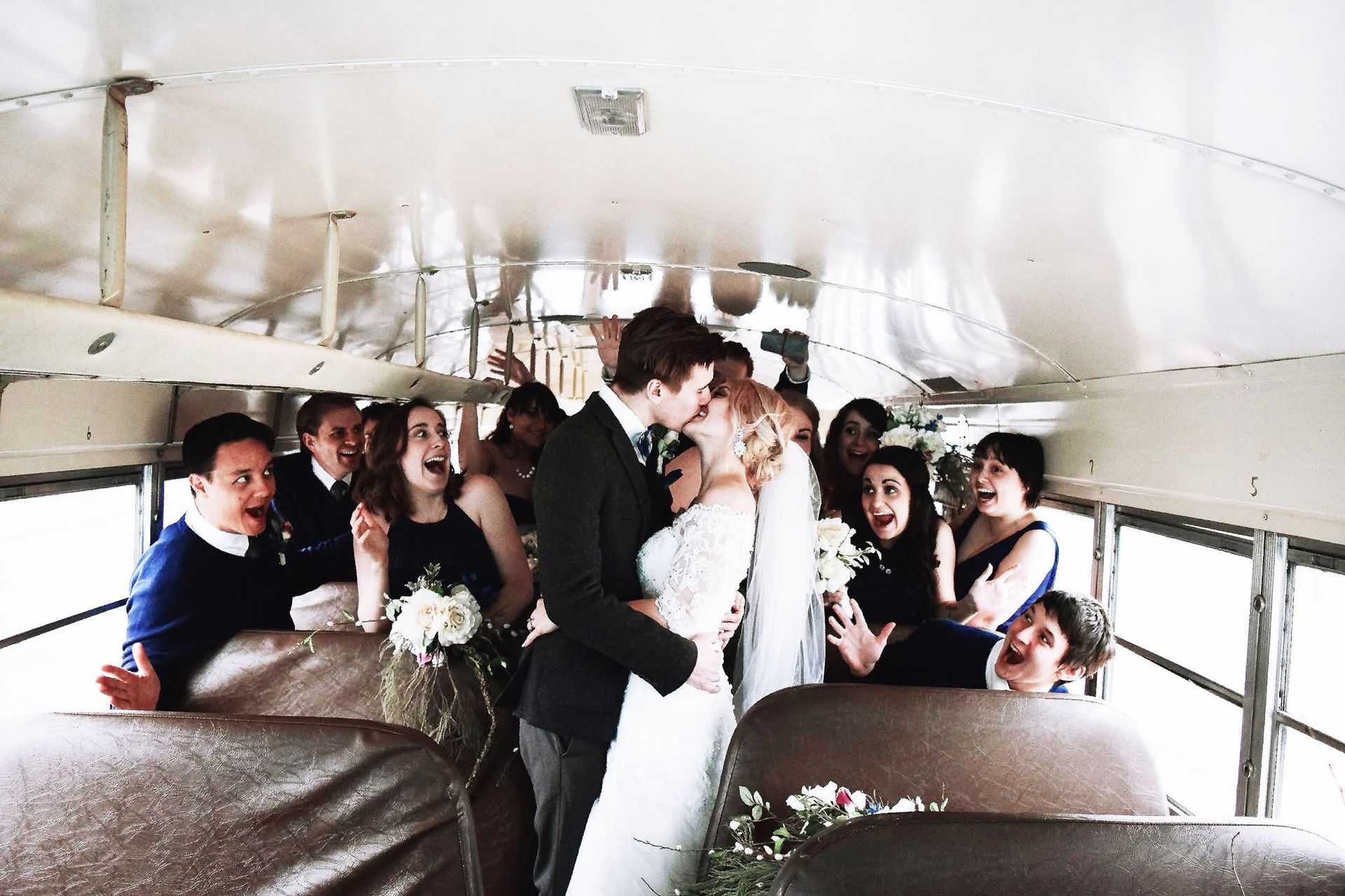 A bride and groom are kissing on a bus with their wedding party.