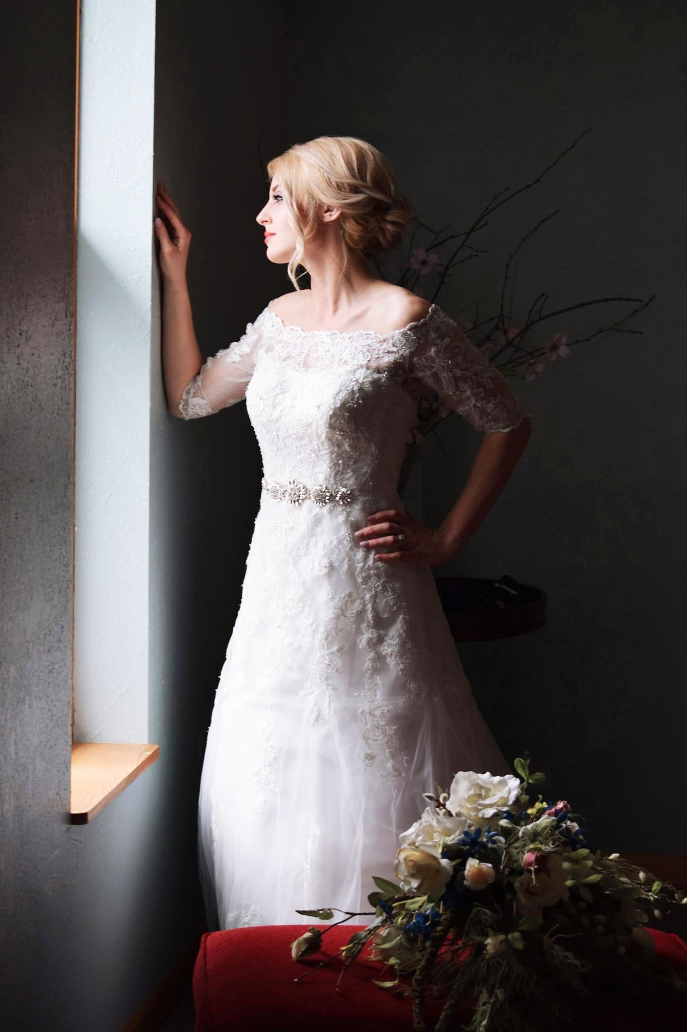 A woman in a wedding dress is standing in front of a window.