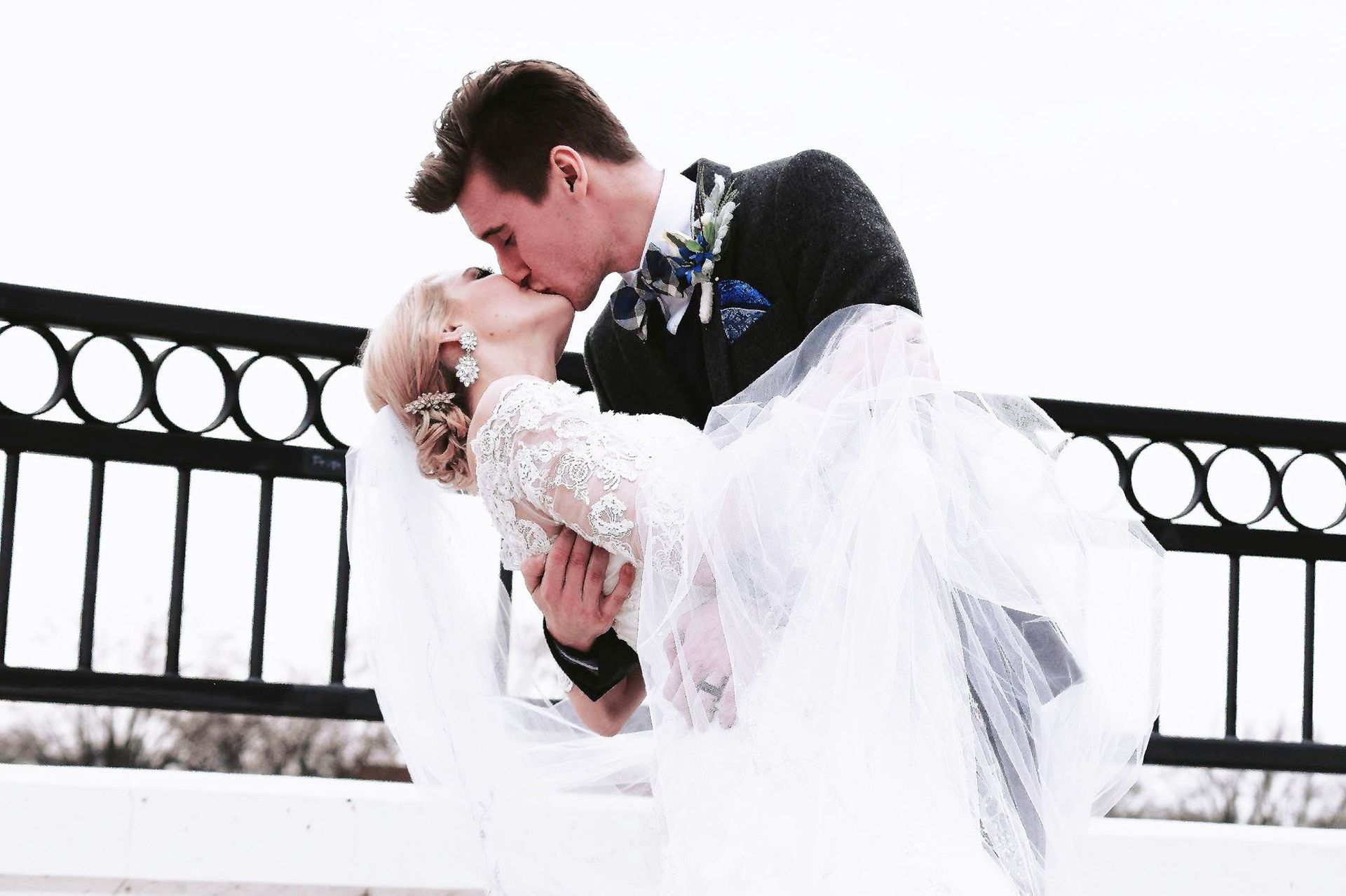 A bride and groom are kissing on a bridge.