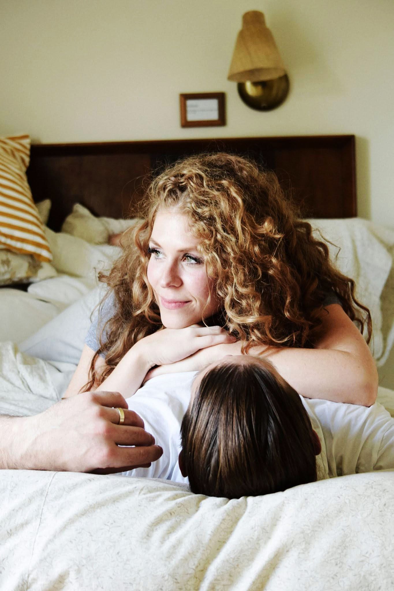 A woman with curly hair is laying on a man 's back on a bed