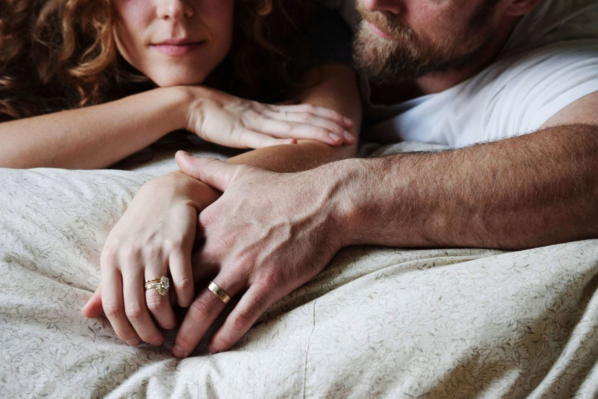 A man and a woman are laying in bed holding hands.
