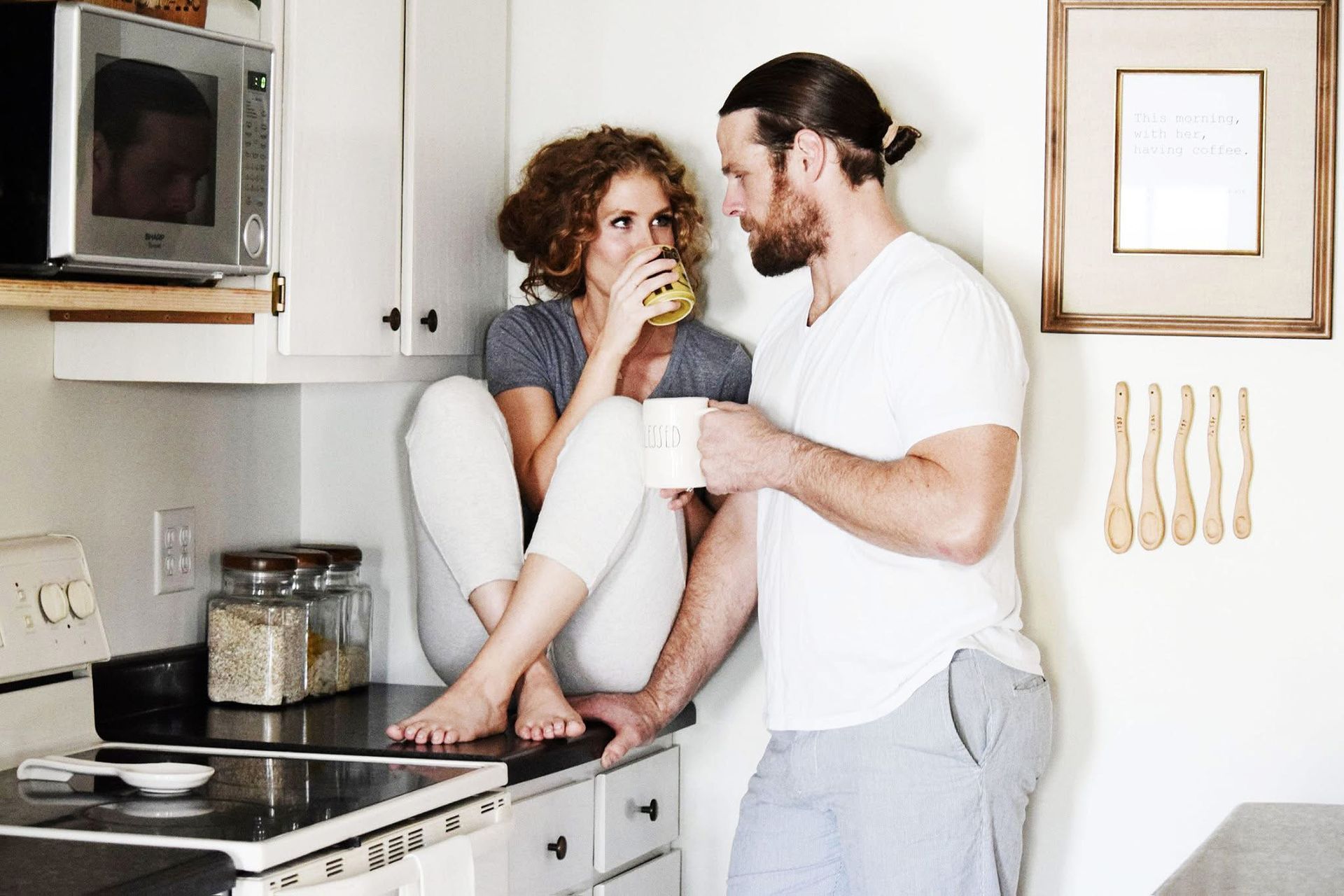 A man and a woman are sitting on a kitchen counter drinking coffee