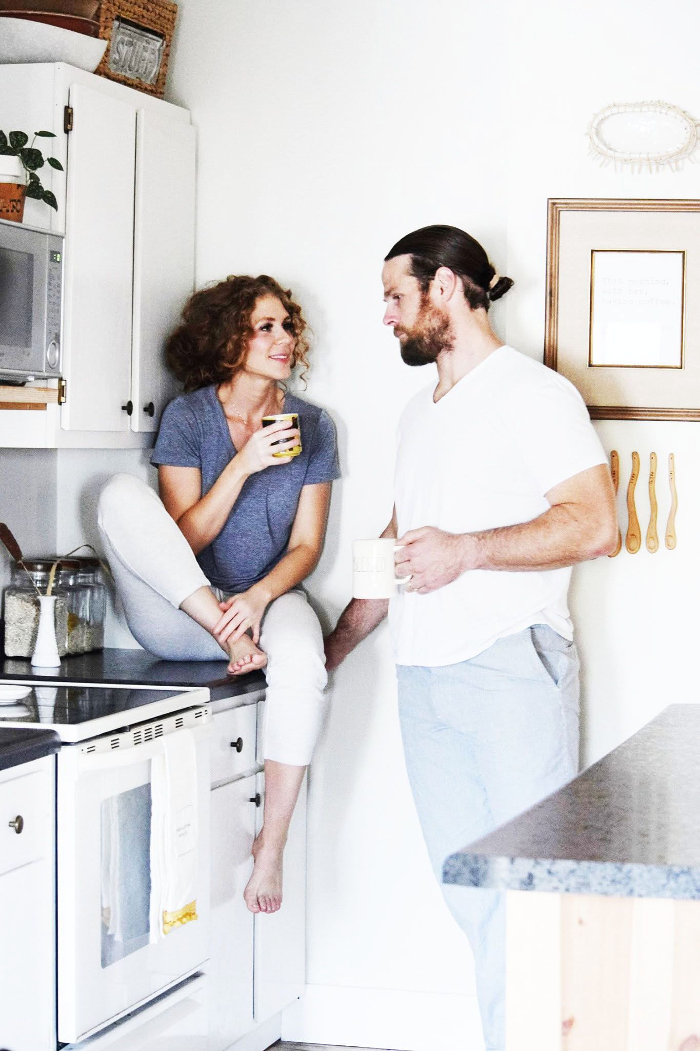 A man and a woman are standing in a kitchen drinking coffee.