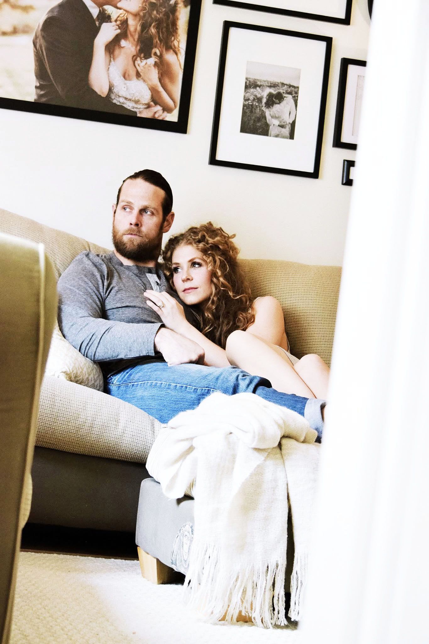 A man and a woman are sitting on a couch looking at pictures on the wall.