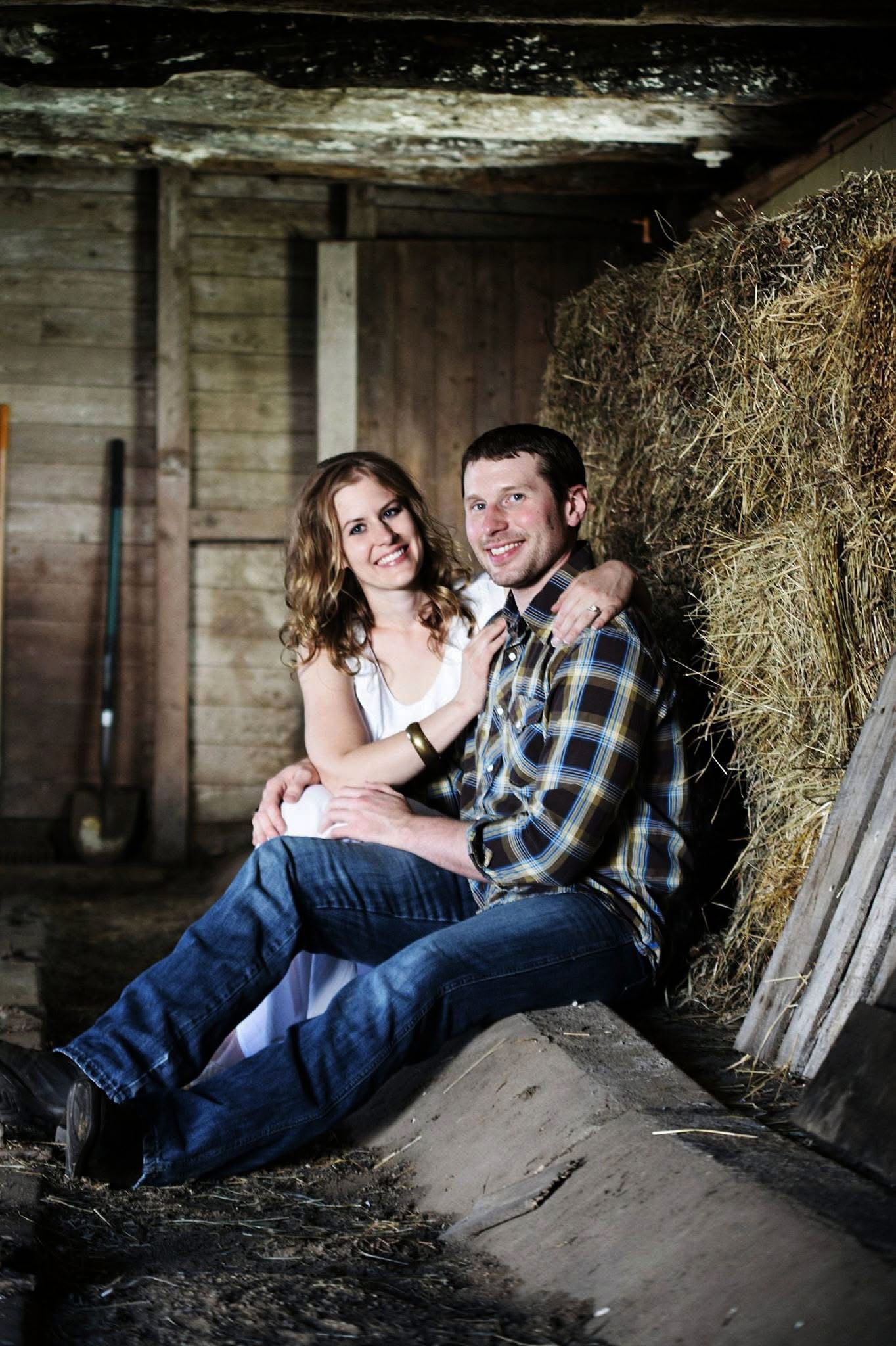 A man and a woman are sitting next to a pile of hay in a barn.