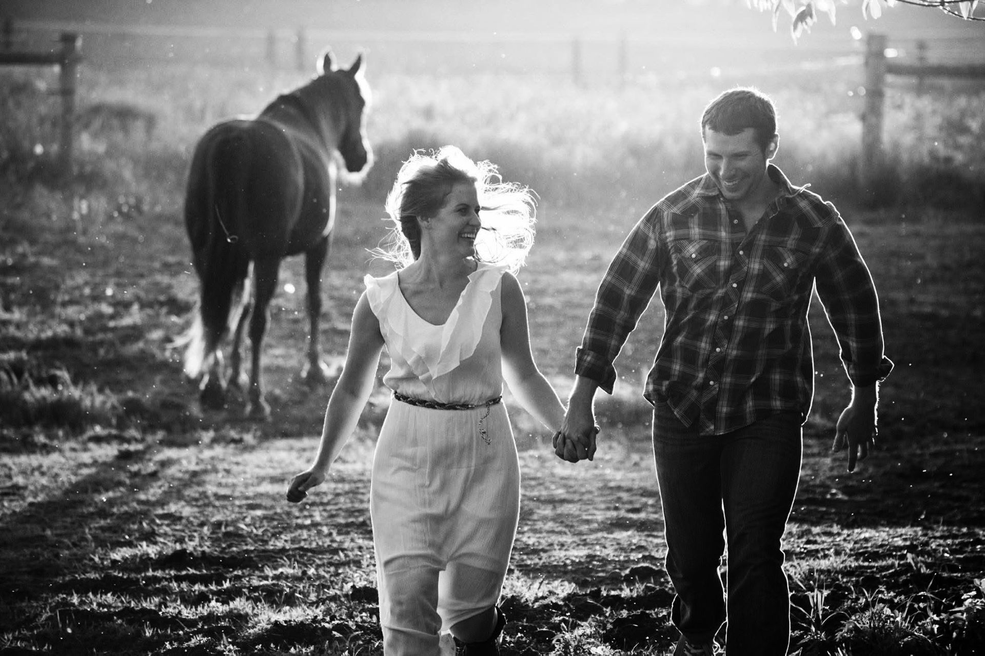 A man and a woman are walking in a field with a horse in the background.