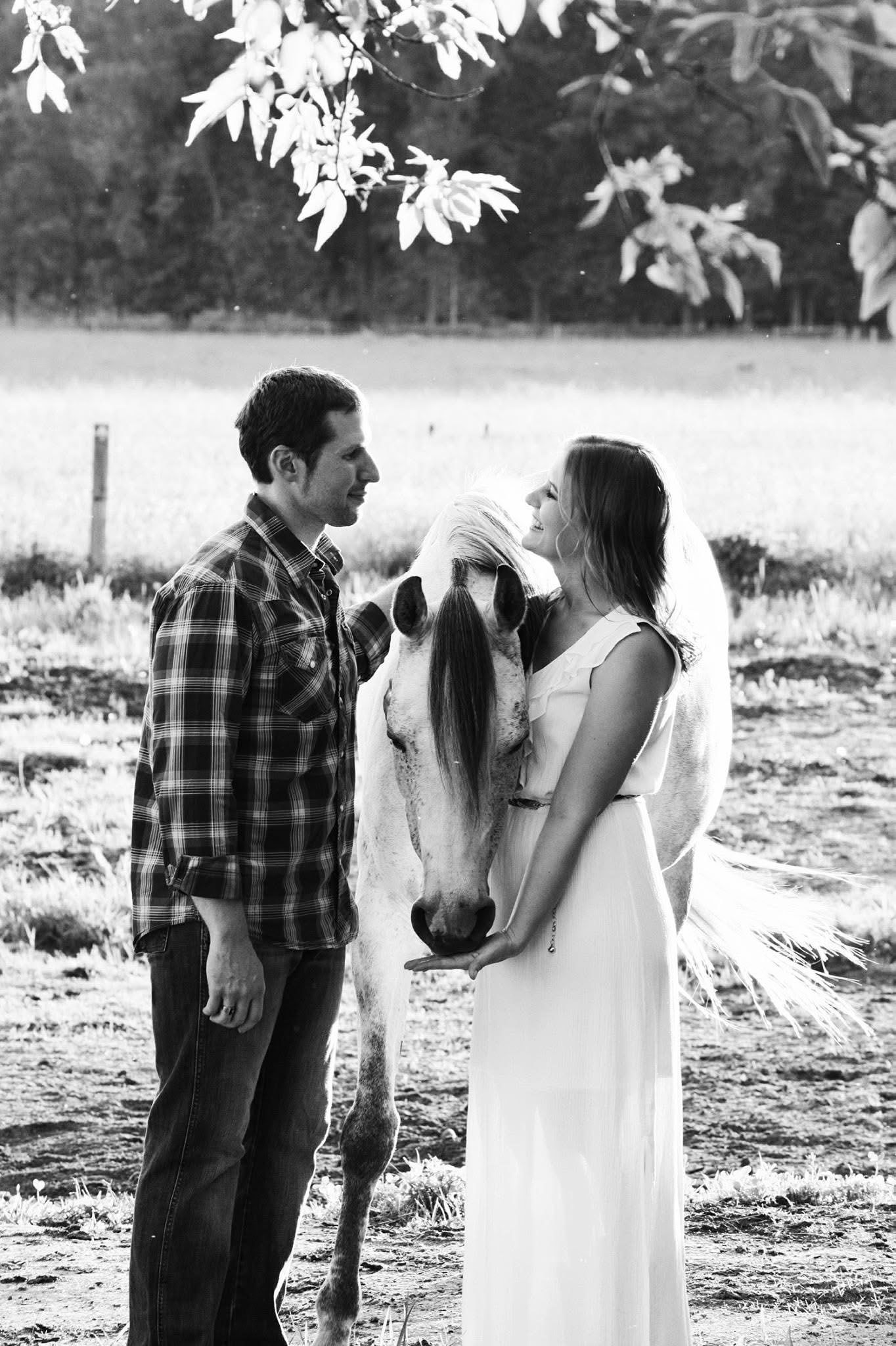 A man and a woman are standing next to a horse in a field.