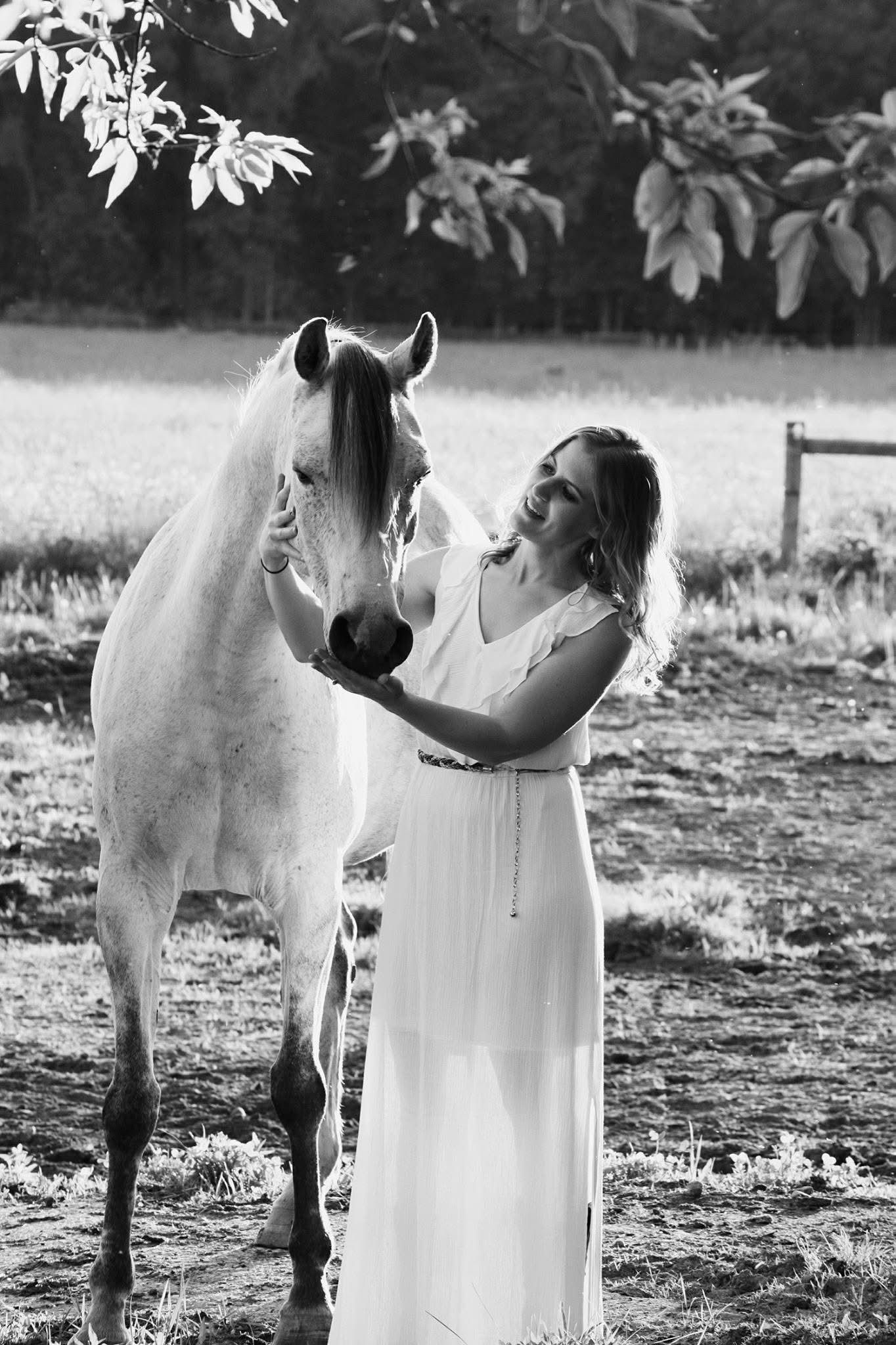 A woman in a white dress is standing next to a white horse.