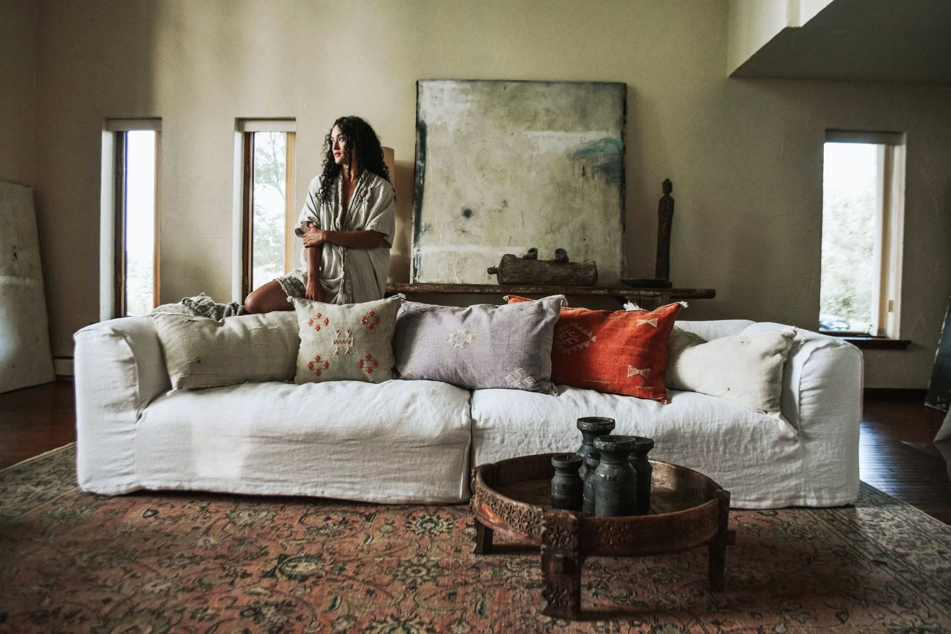 A woman is standing next to a white couch in a living room.