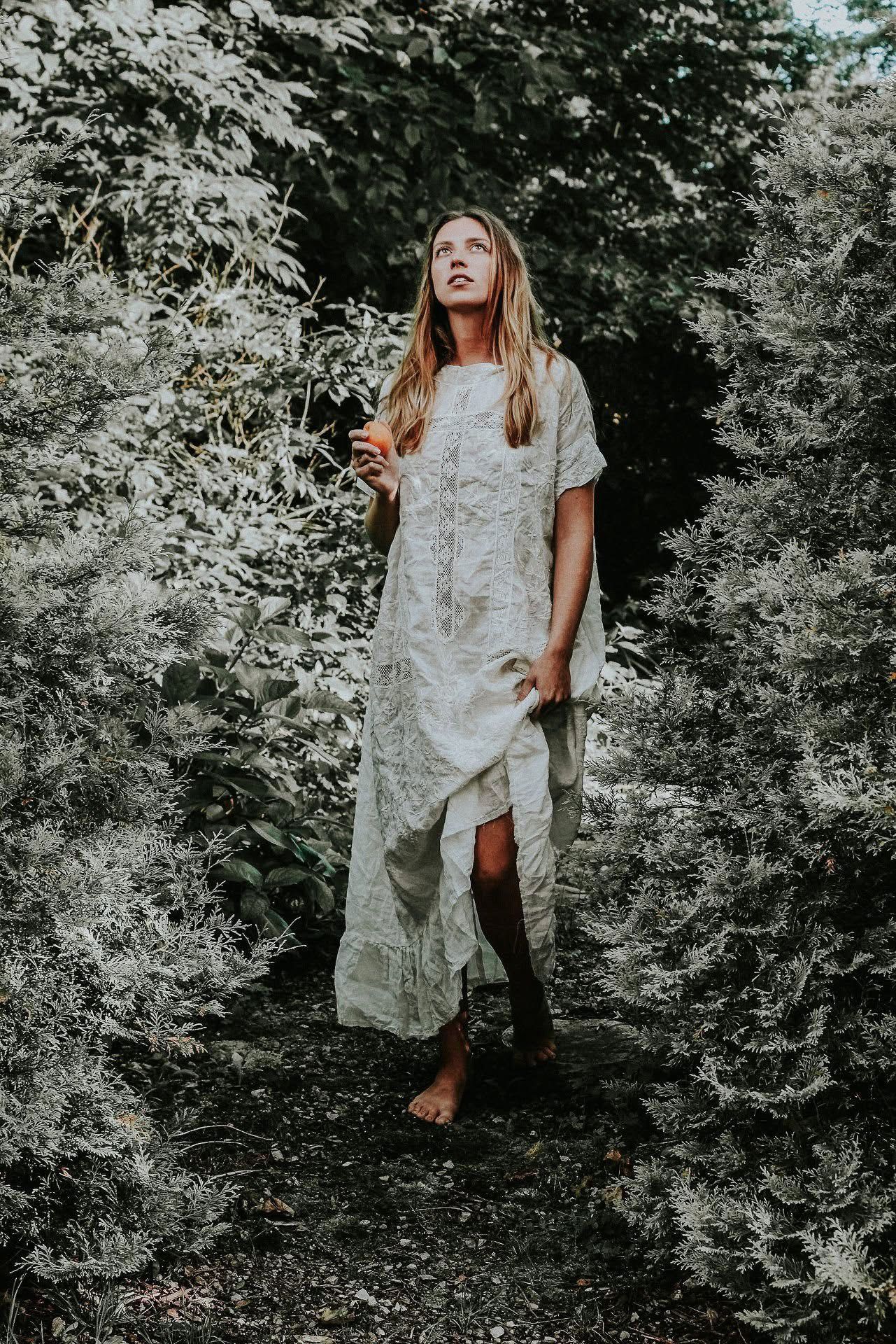 A woman in a white dress is standing in the woods.