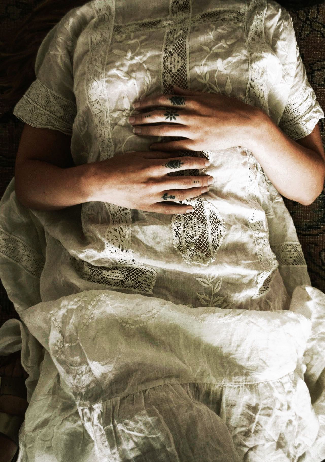 A woman in a white dress is laying on a bed with her hands on her belly.
