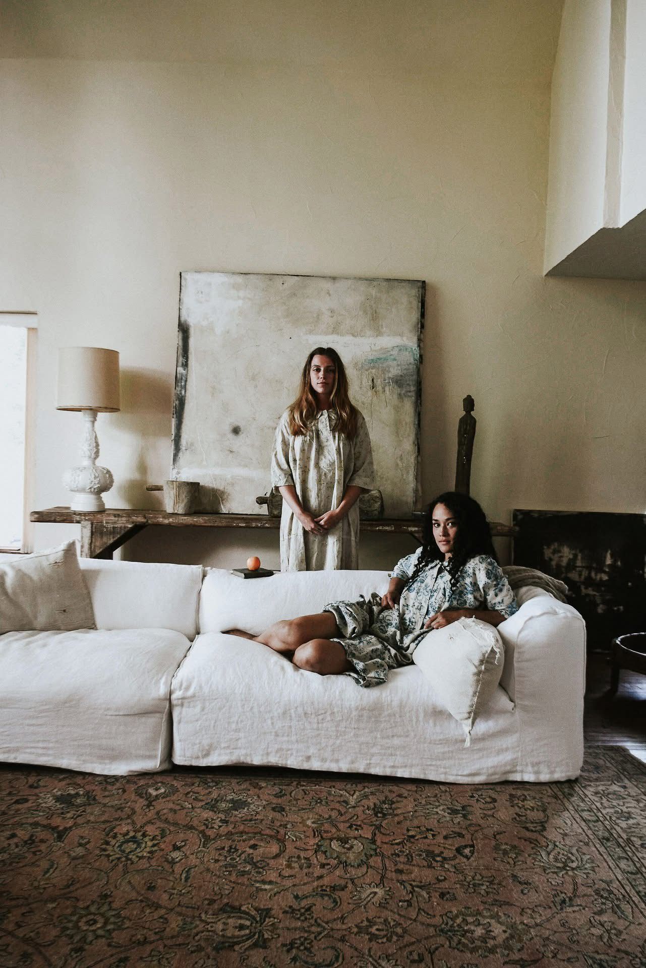Two women are sitting on a white couch in a living room.