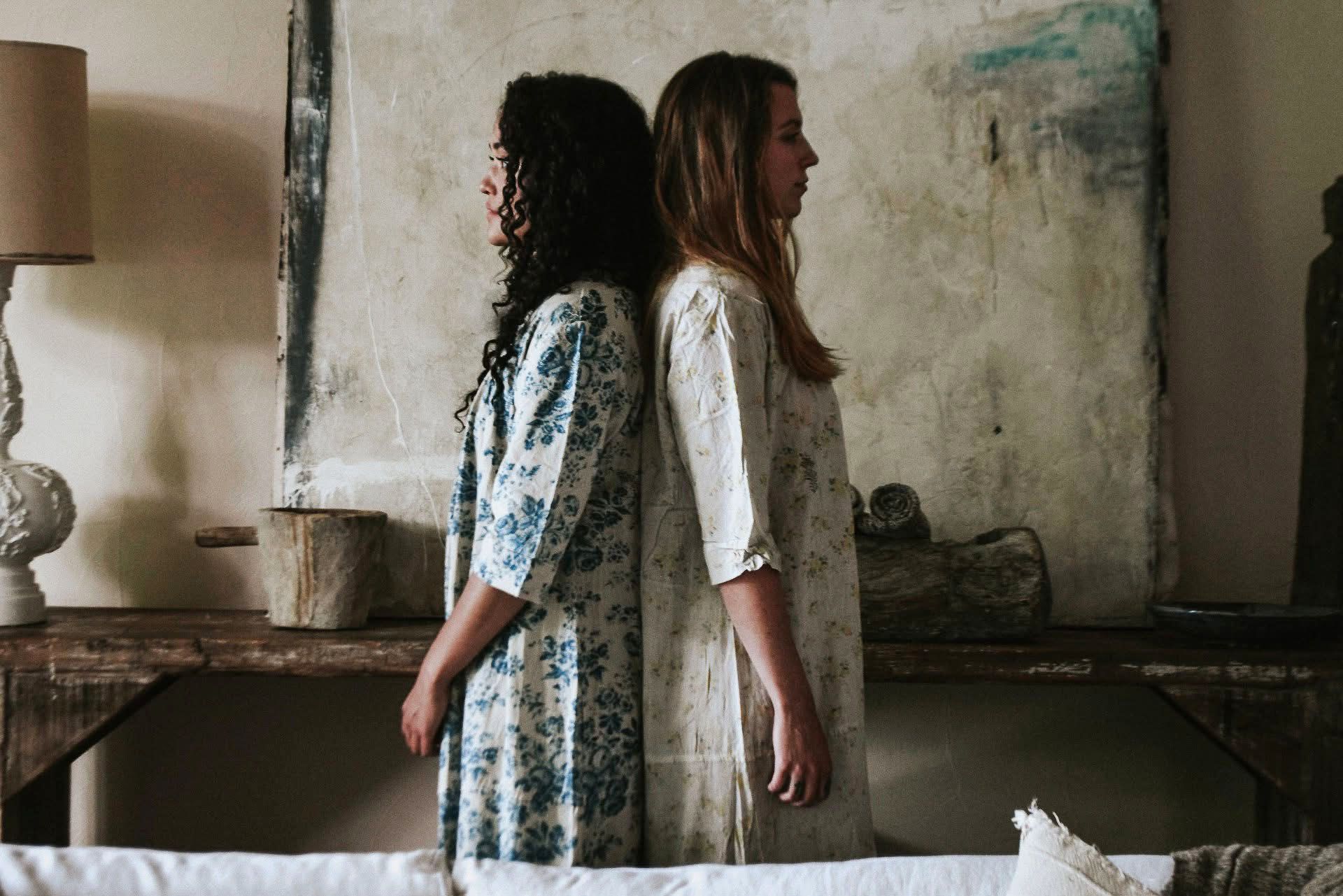 Two women are standing back to back in a living room.