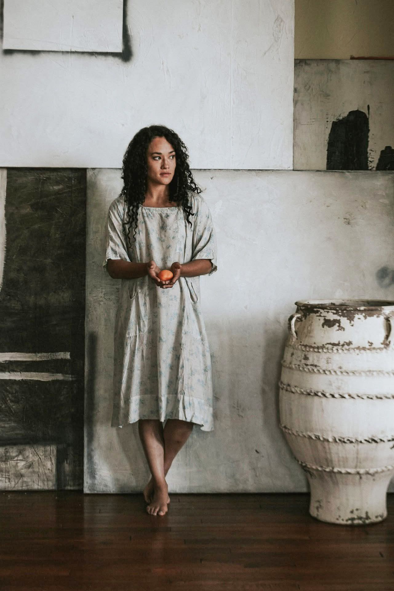 A woman in a dress is standing next to a vase in a room.
