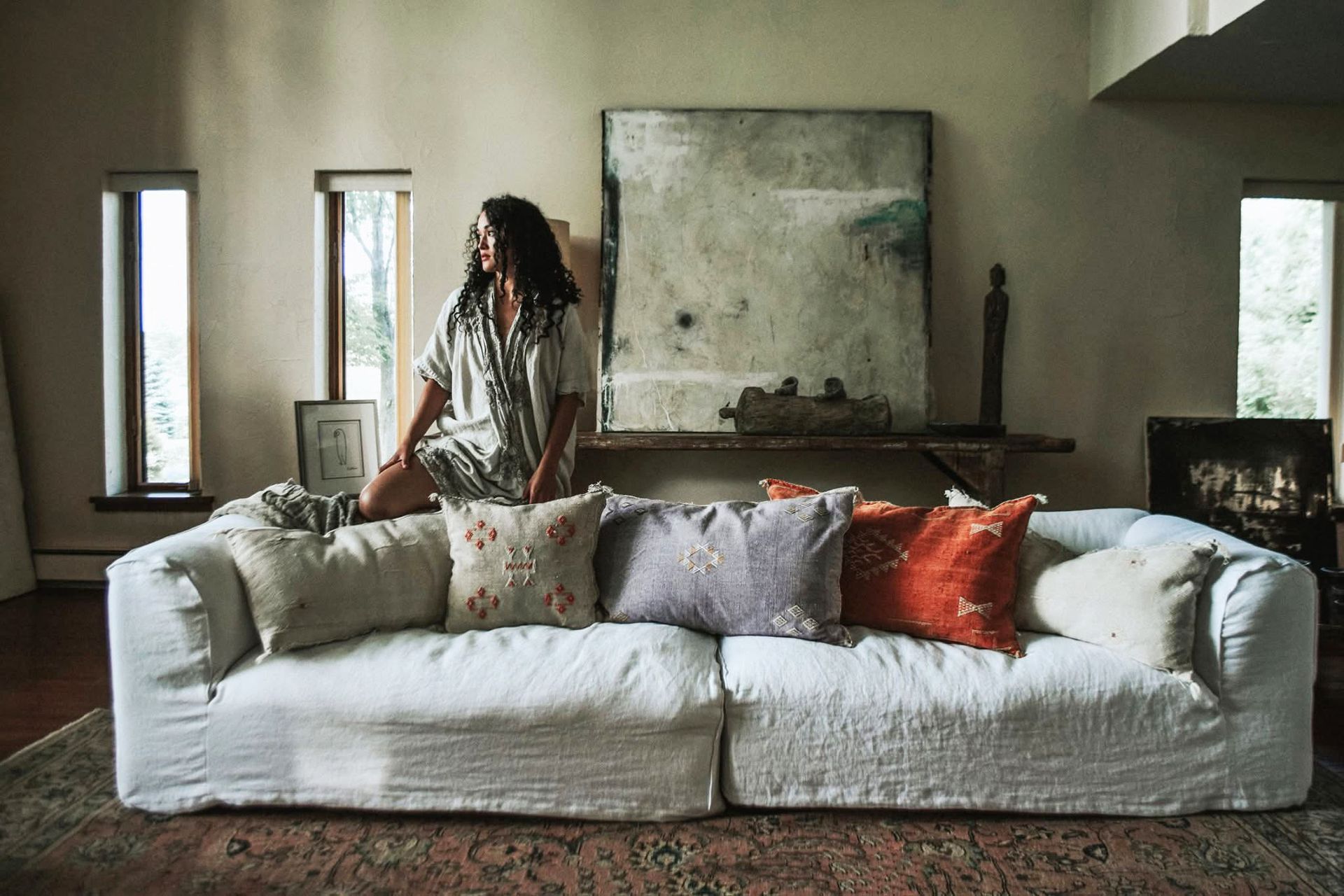 A woman is sitting on a white couch in a living room.