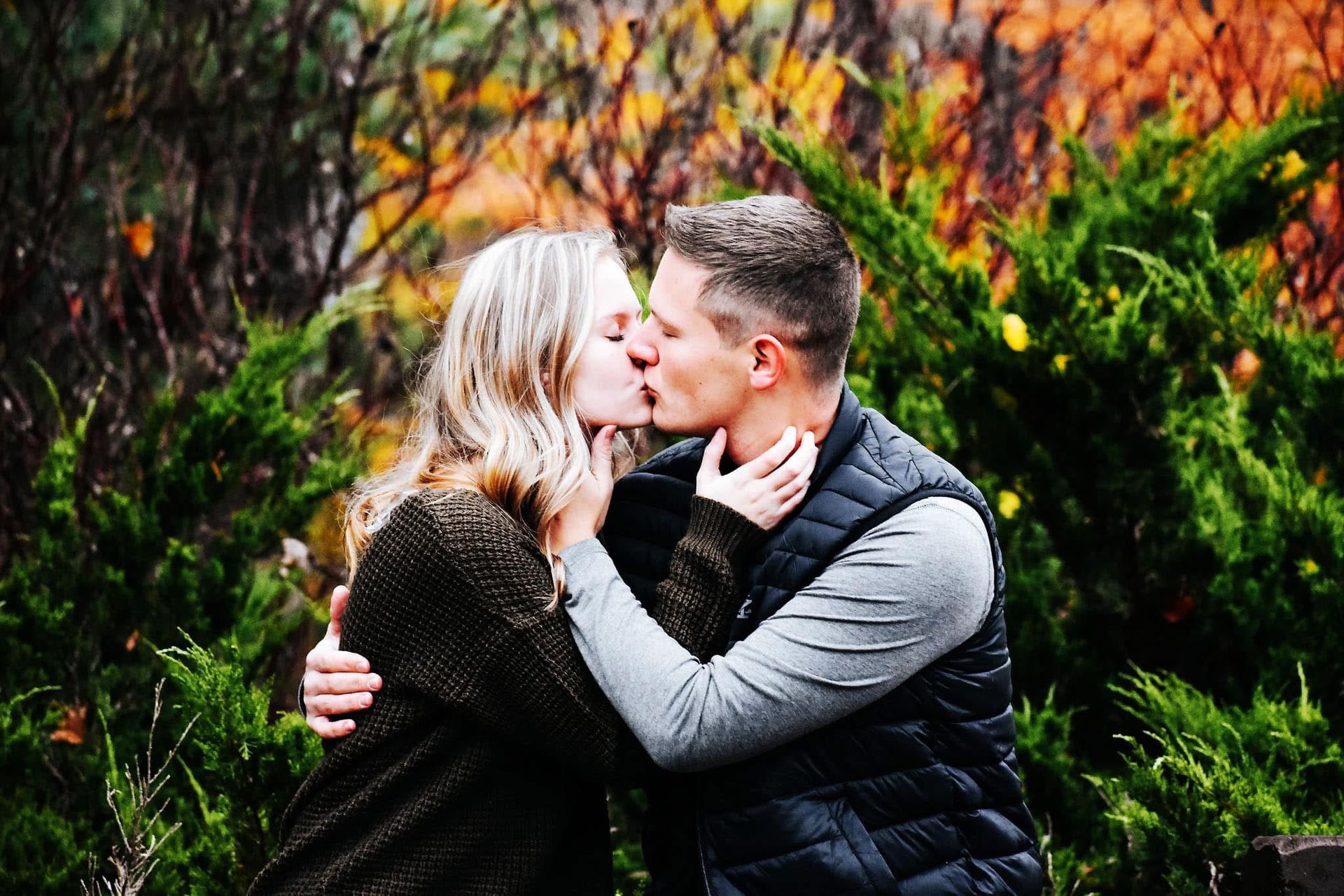 A man and a woman are kissing in a park.