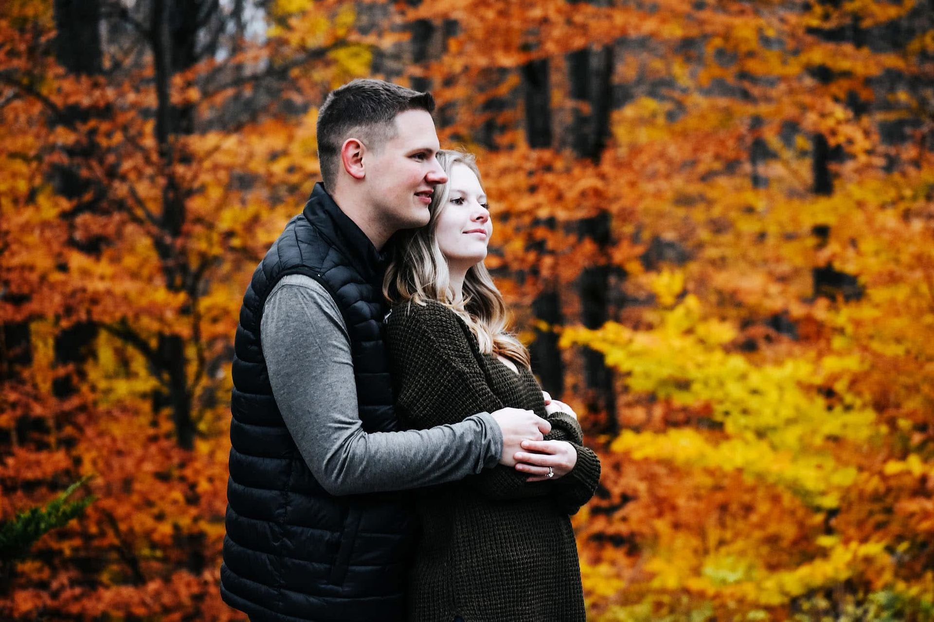 A man and a woman are hugging in the woods.