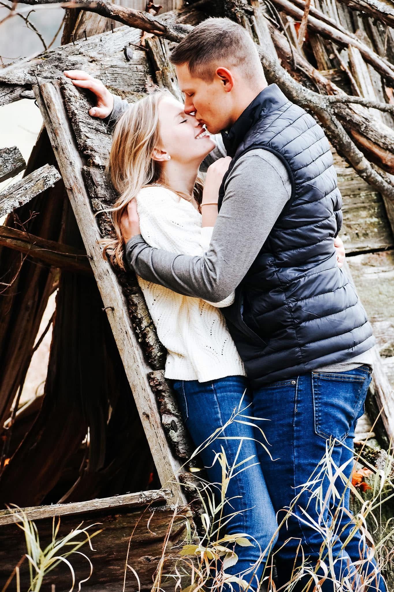 A man and a woman are kissing in front of a wooden structure.