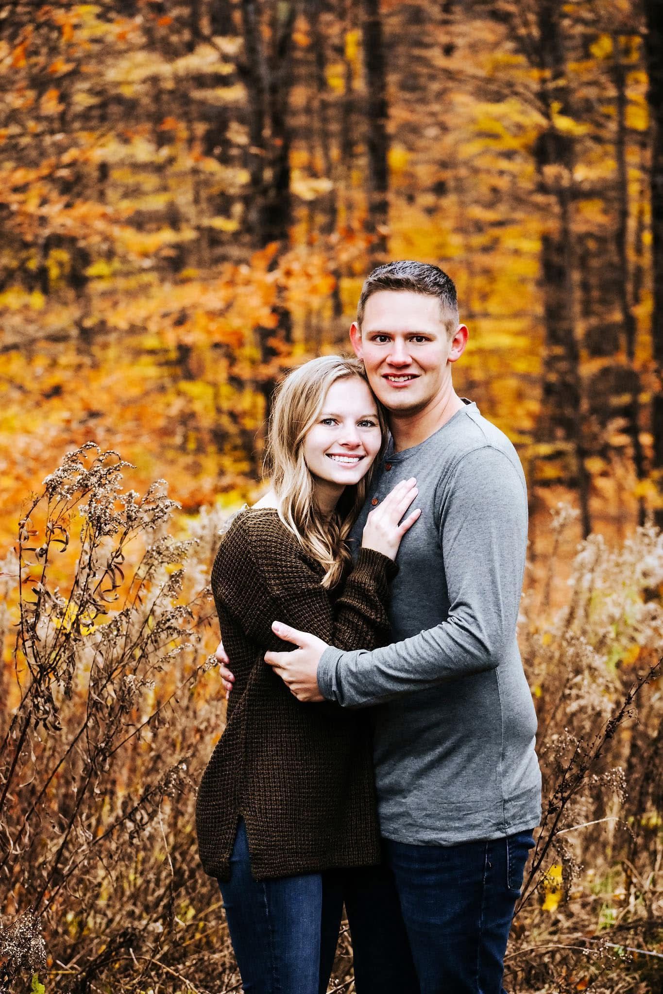 A man and a woman are posing for a picture in the woods.