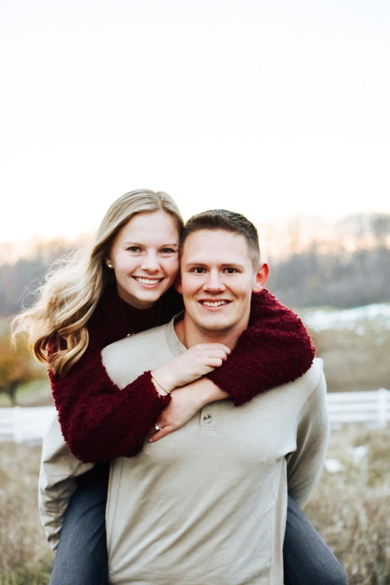 A man is carrying a woman on his back in a field.